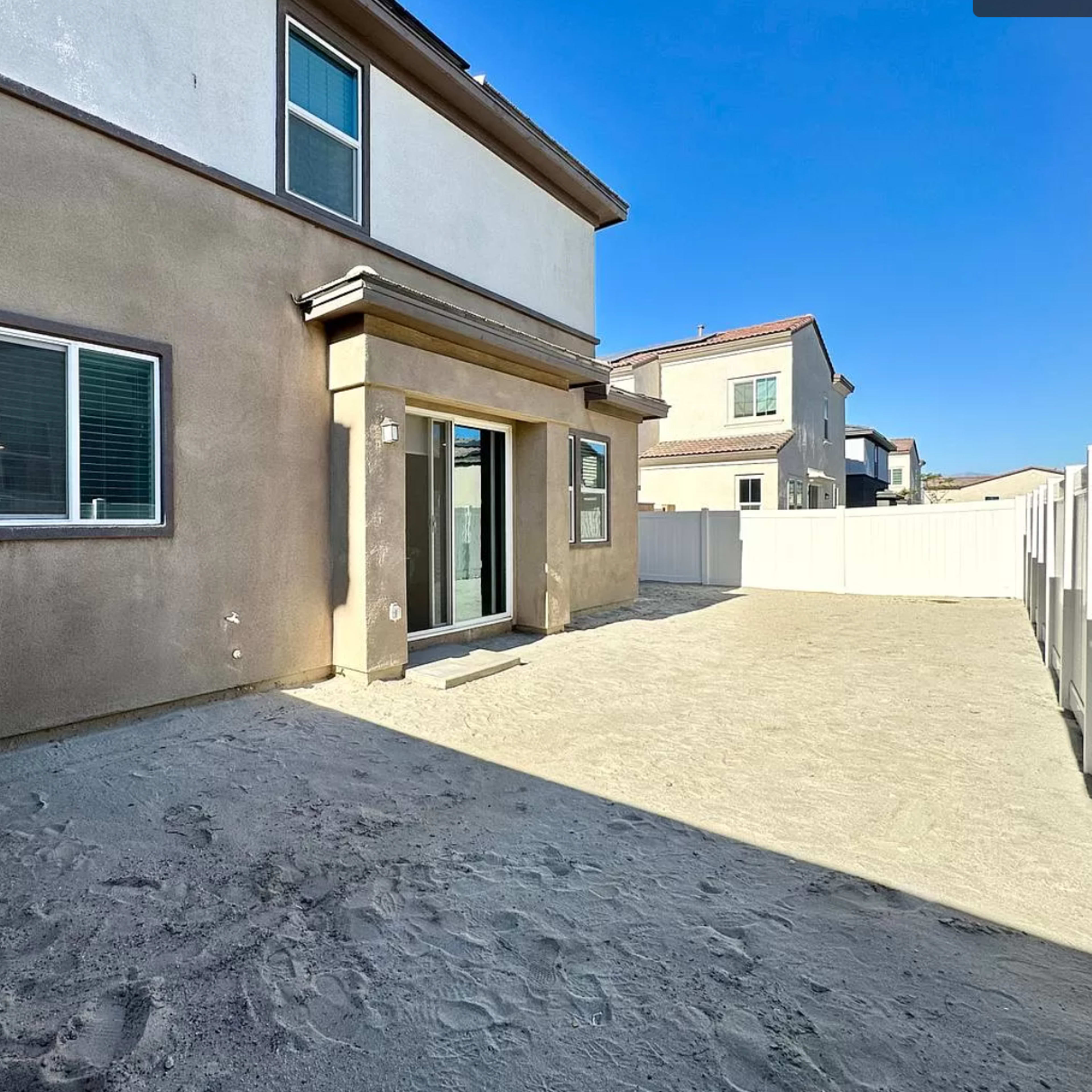 The back exterior of a two-story house with a clean, sandy yard and a fenced area.