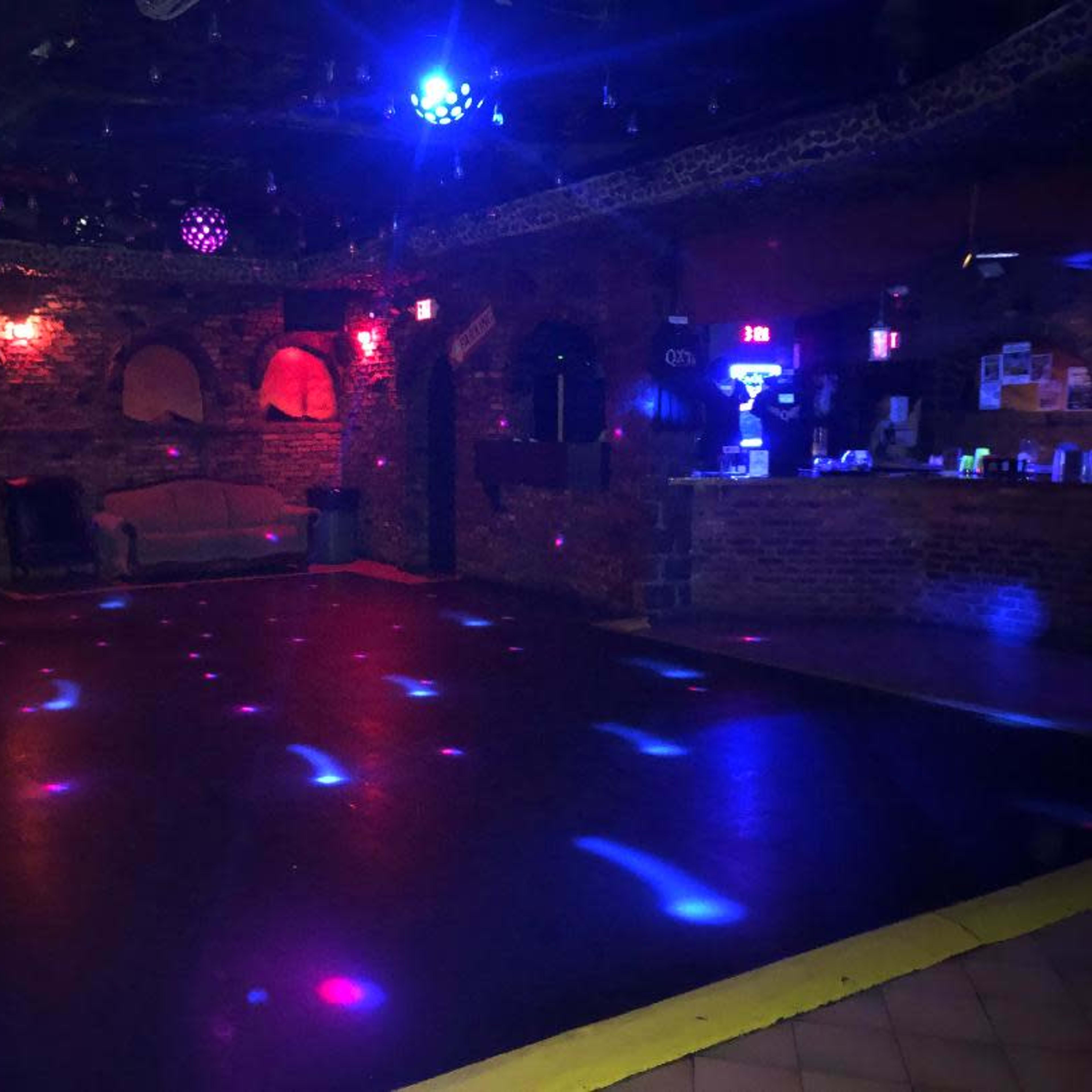 An empty dance floor in a dimly lit venue with brick walls and colorful light spots scattered across the floor.
