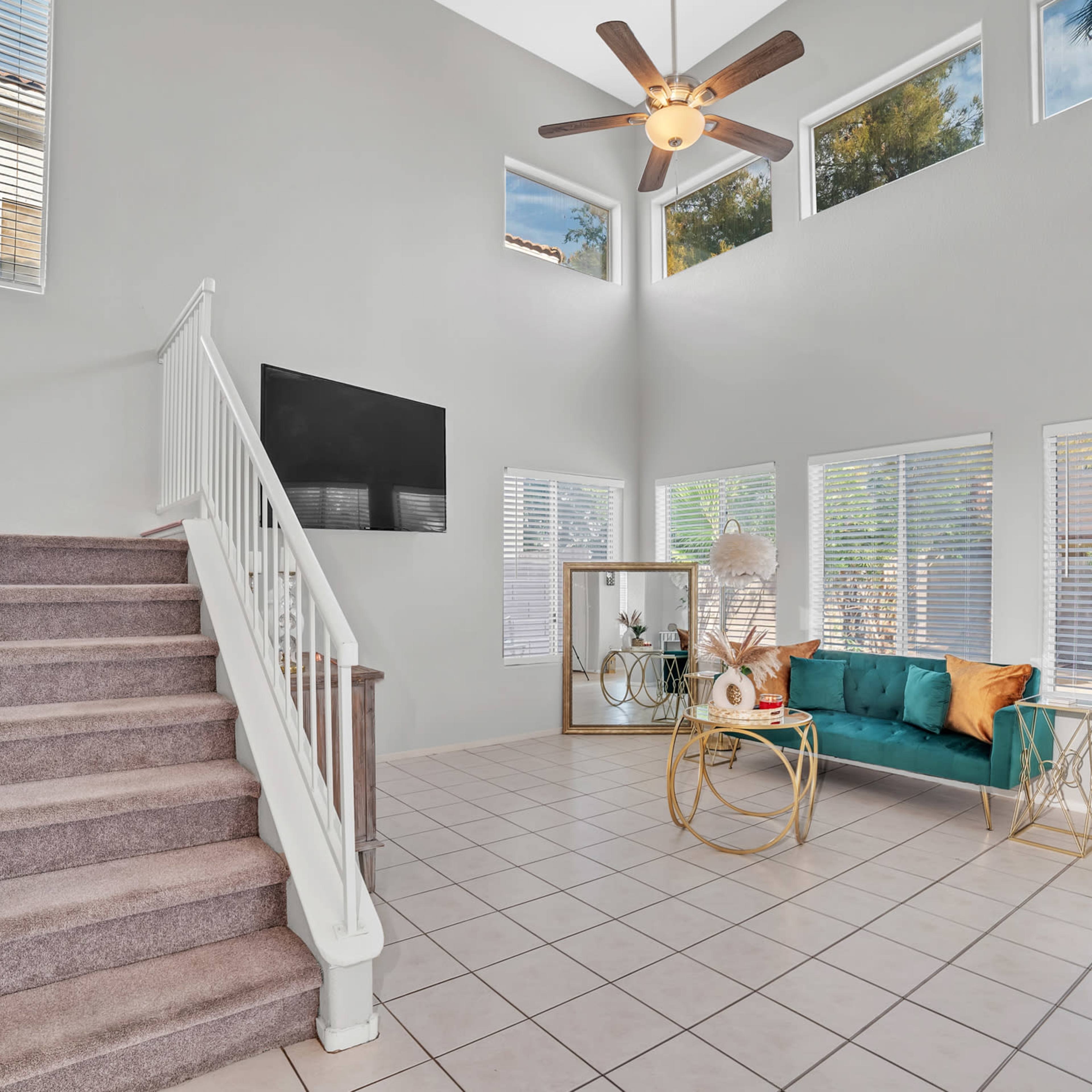 A spacious living area with a staircase, large windows, and a green sofa paired with decorative accents.