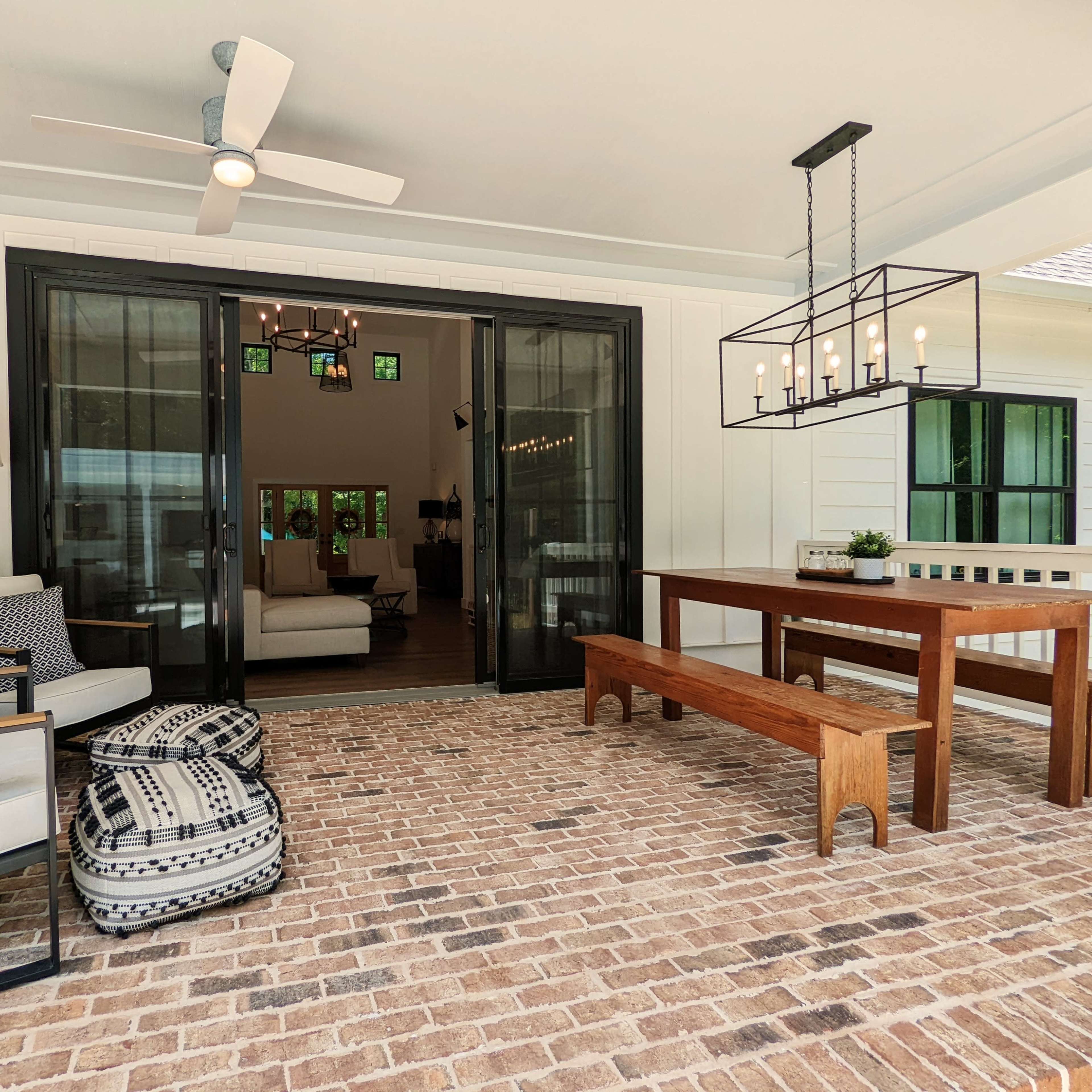 A covered outdoor patio with a dining table, seating, and a view of an interior living space through large sliding glass doors.