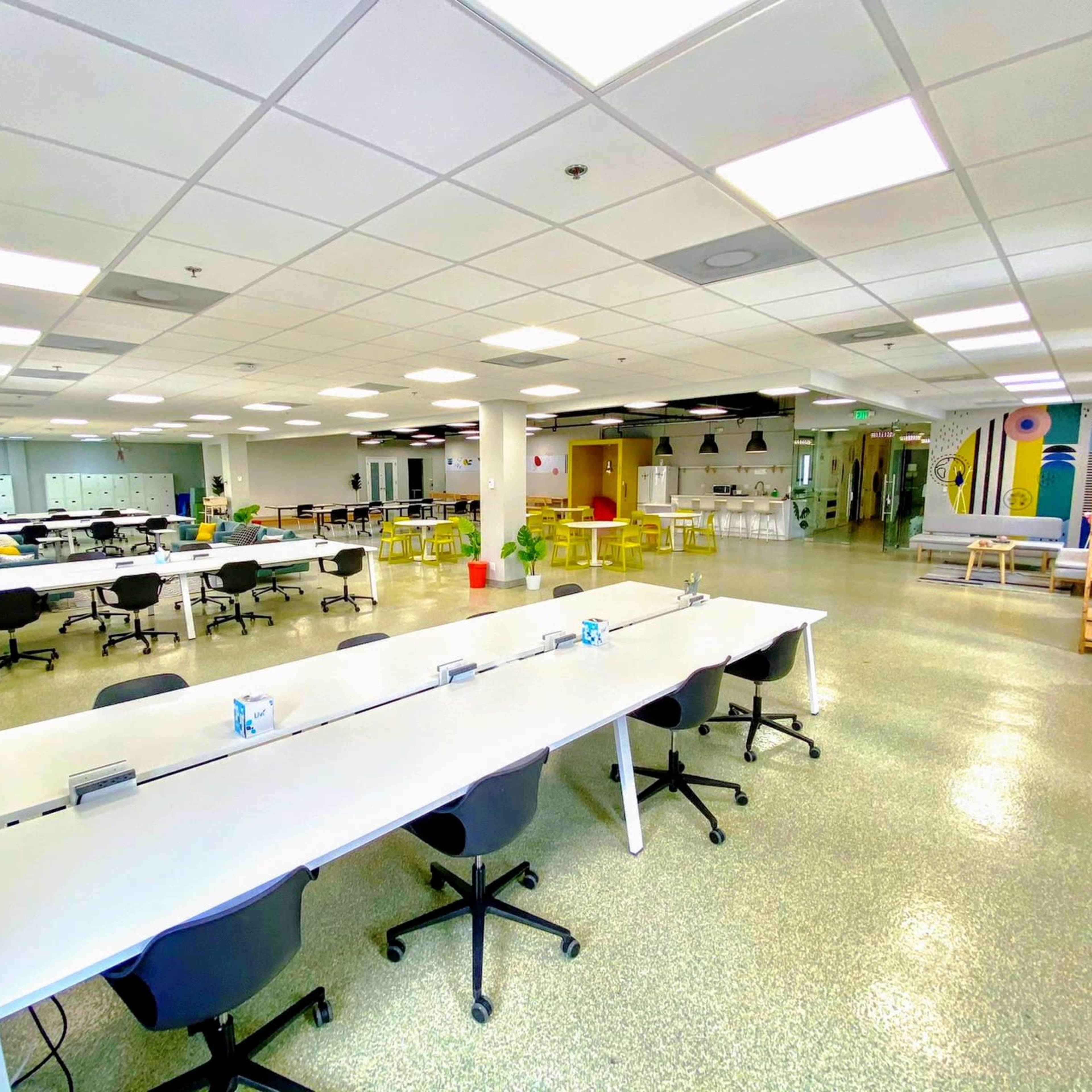 A spacious, well-lit office area with multiple long white tables and black chairs arranged in rows.