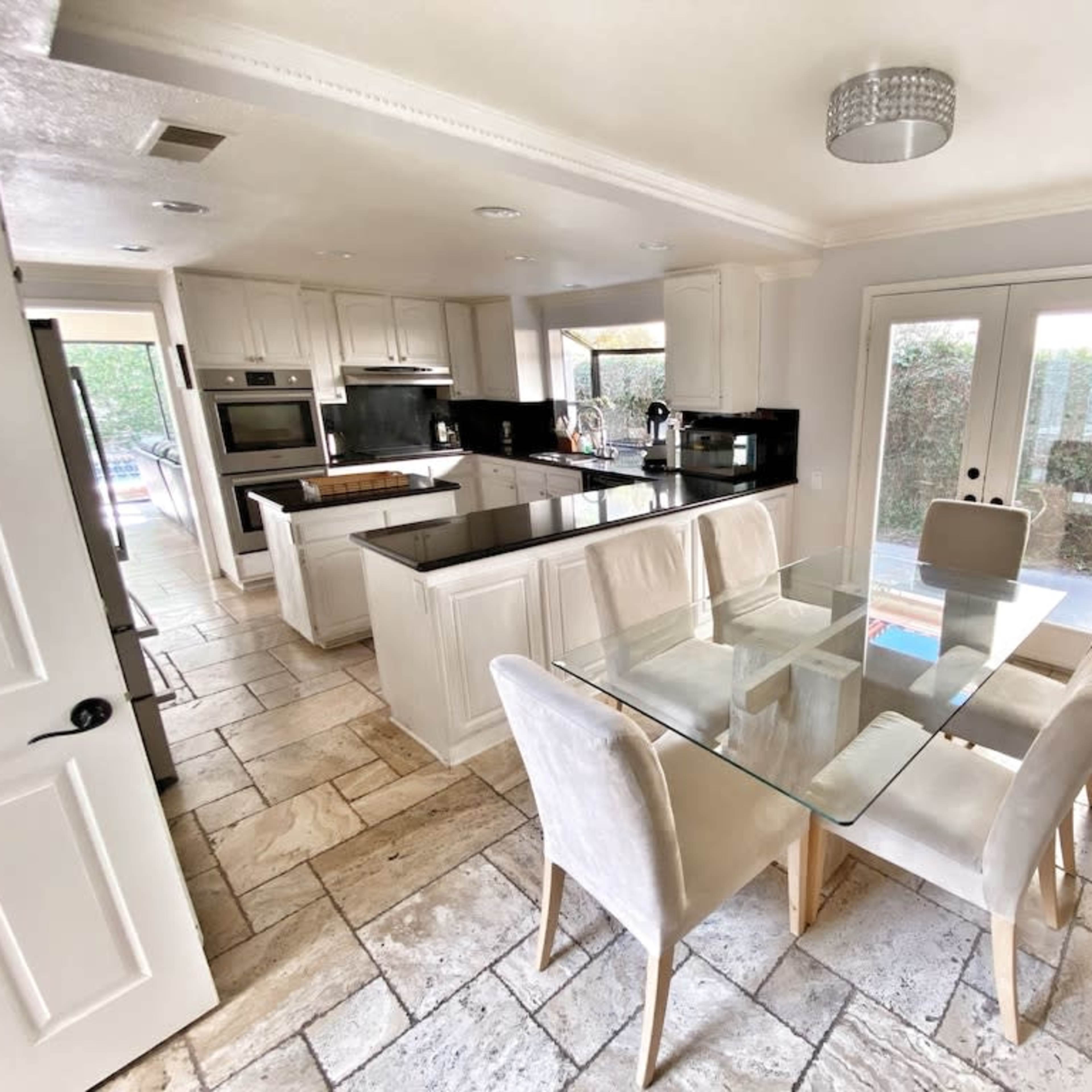 A modern kitchen and dining area with white cabinetry, a glass dining table, and tiled floors.