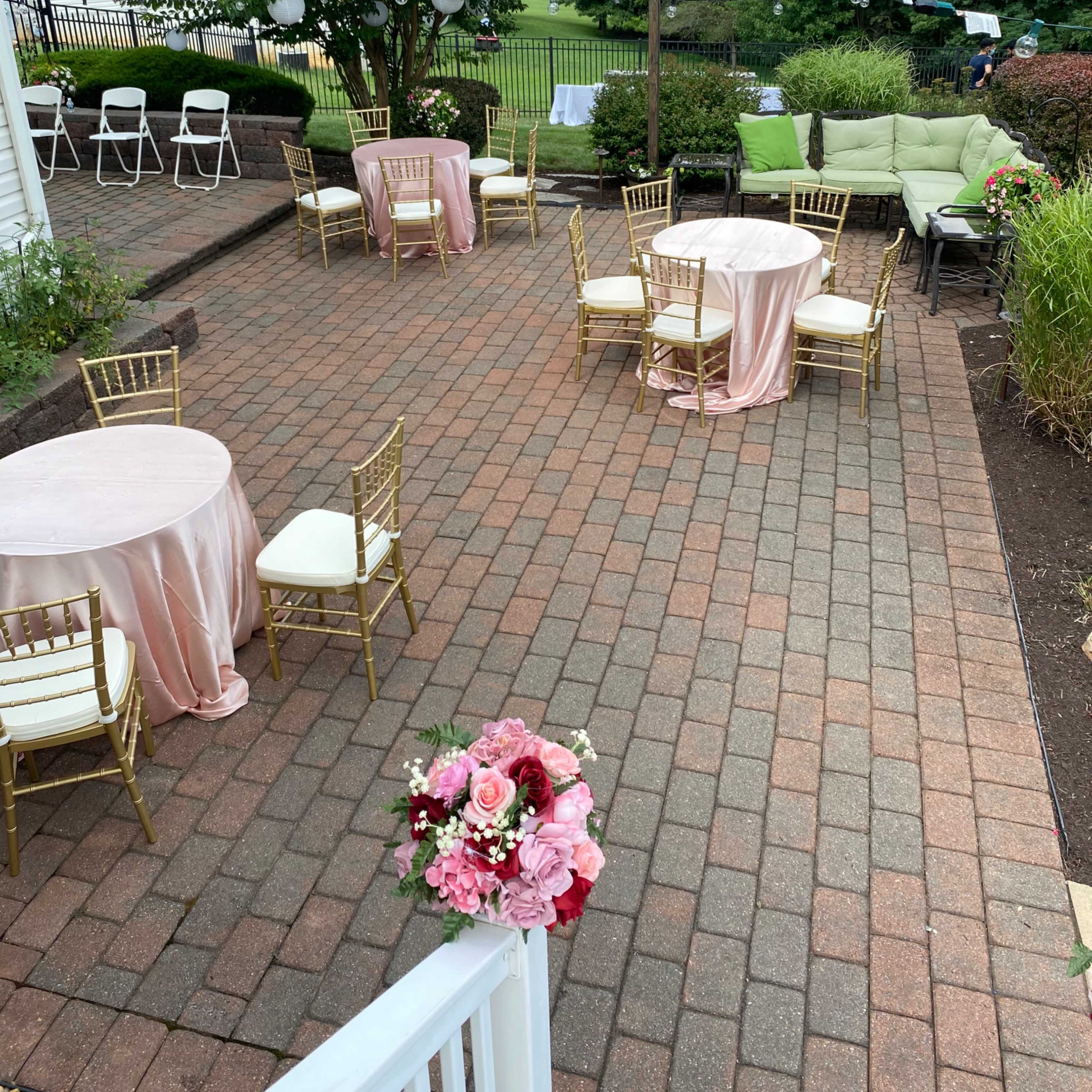 An outdoor patio area with round tables draped in pink tablecloths and gold chairs set up for an event.