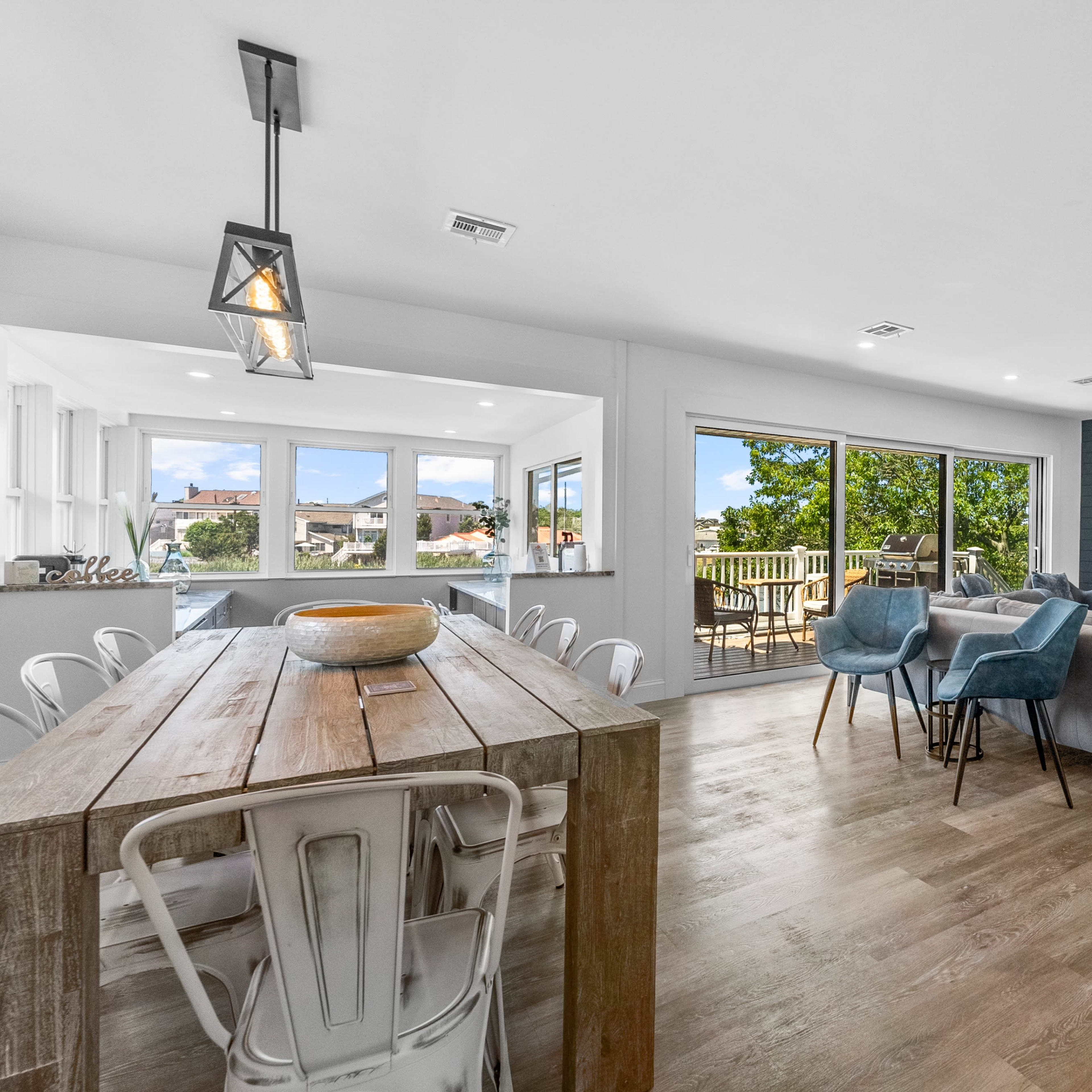 A modern open-concept living and dining area with large windows, a wooden dining table, and a cozy seating arrangement beside a fireplace.