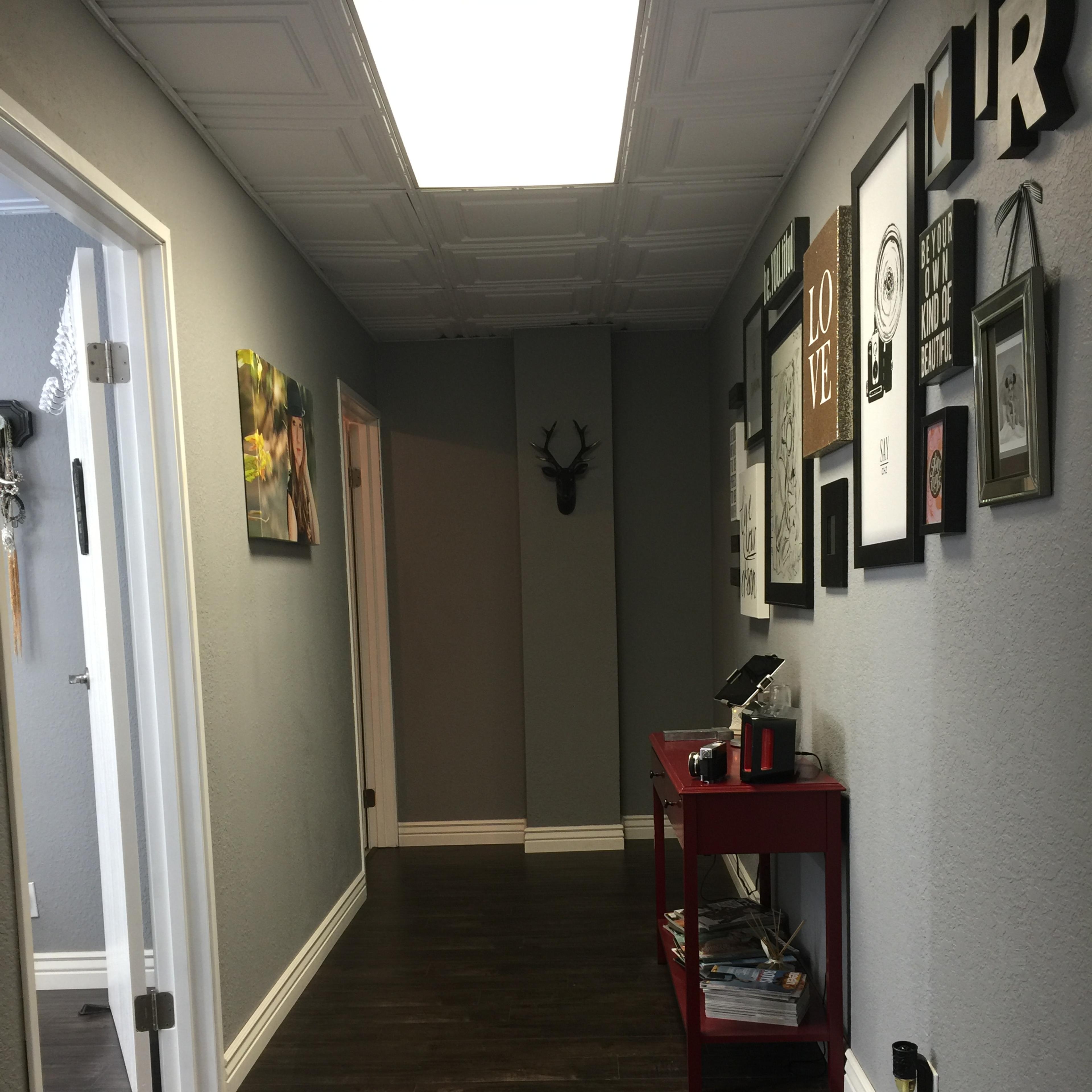 A hallway with gray walls, wooden flooring, framed art on the walls, and a red table on the right side.