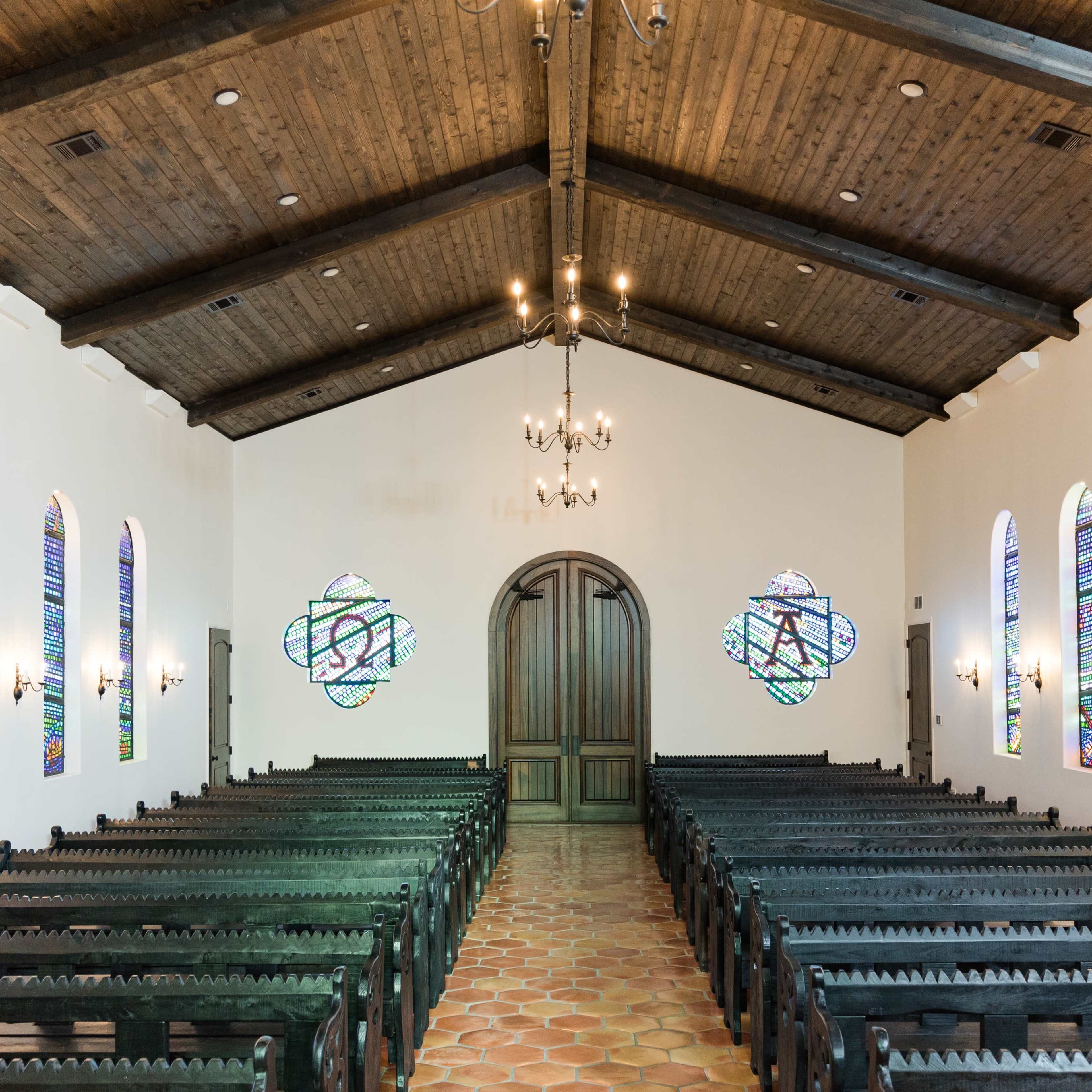 The interior of a church features rows of black wooden pews, colorful stained glass windows, and a wooden beam ceiling.