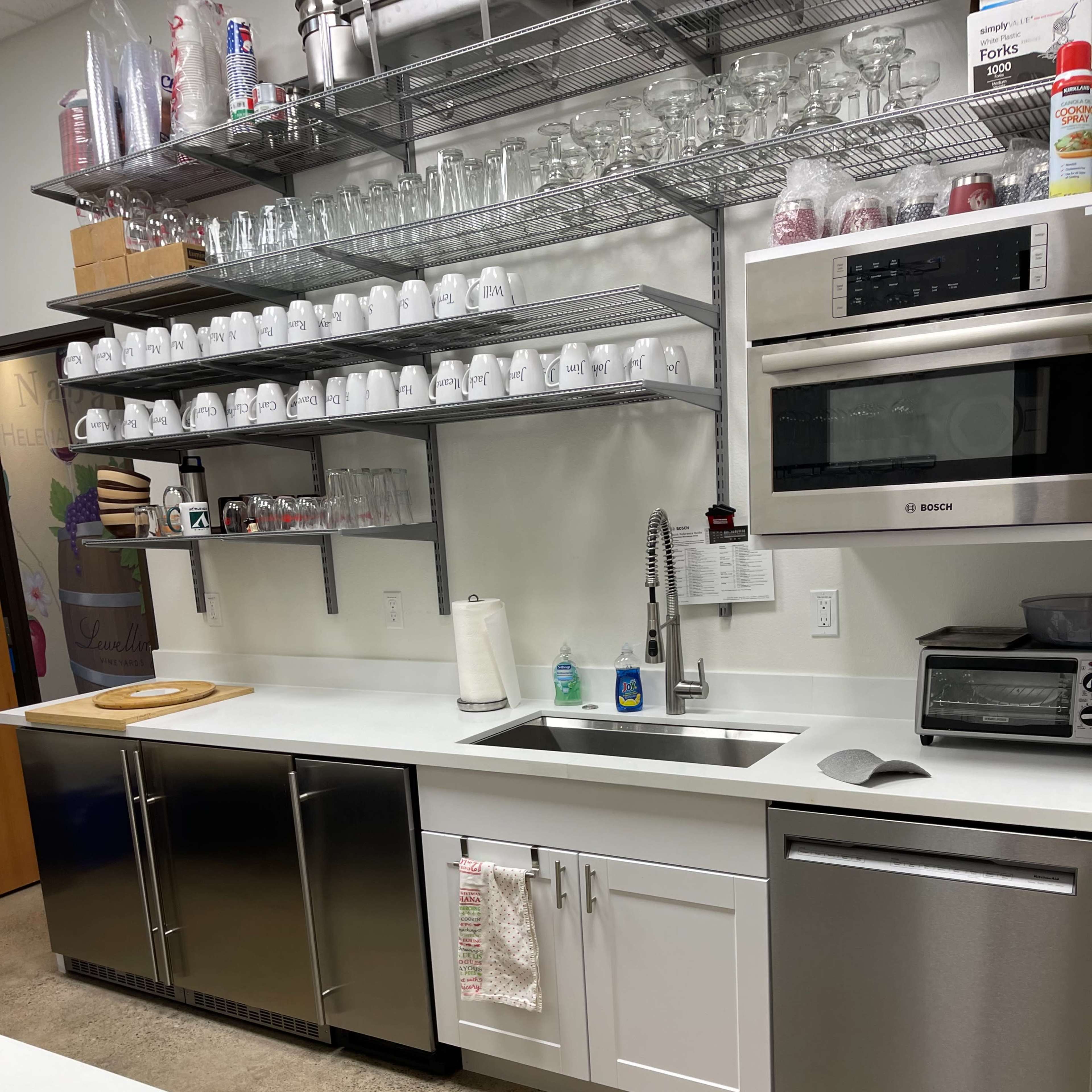 A modern kitchen with stainless steel appliances, white cabinets, a large sink, and shelves holding glasses and dishes.
