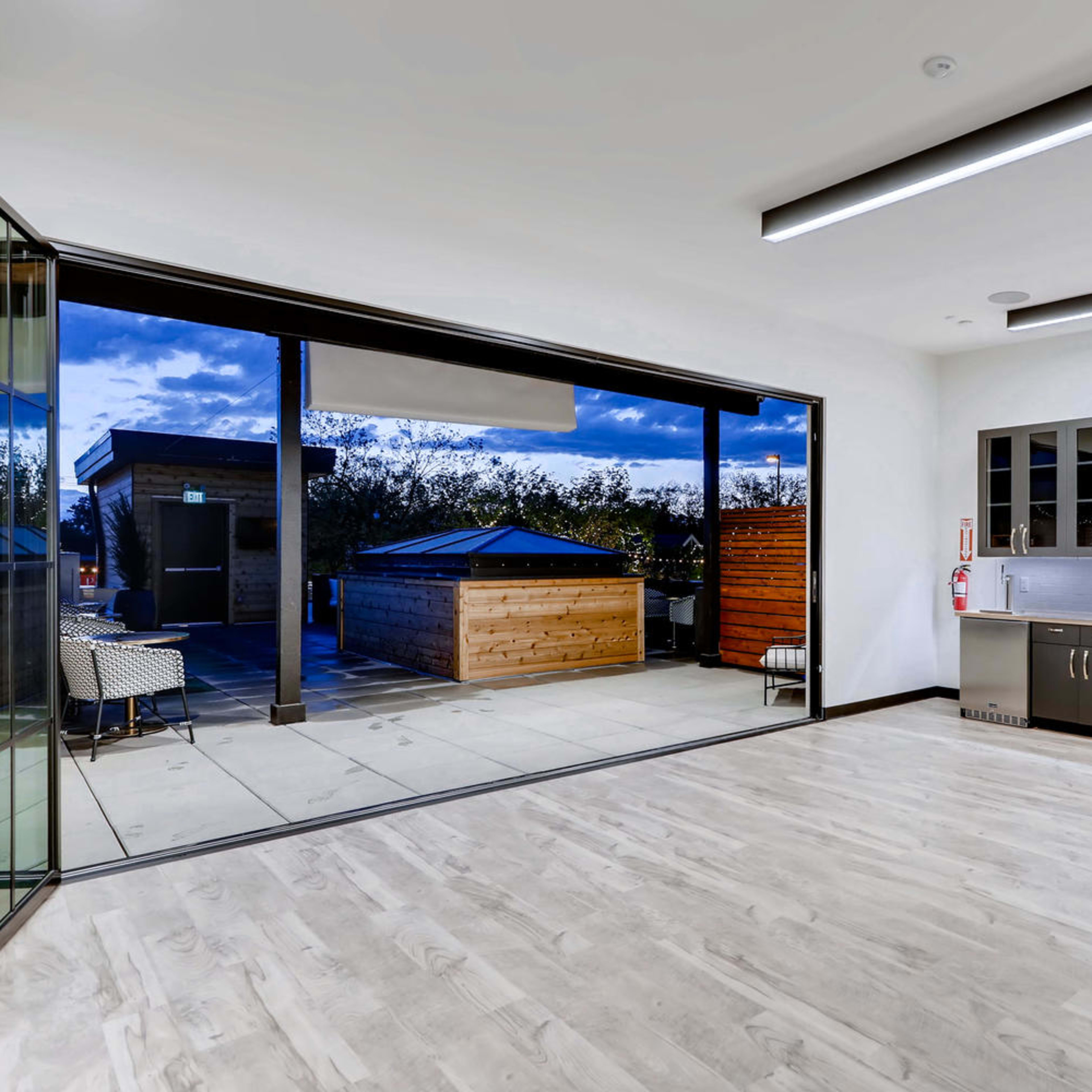 A modern interior space with large glass doors opening to a patio, featuring a kitchen area with sleek cabinetry and stainless steel appliances.