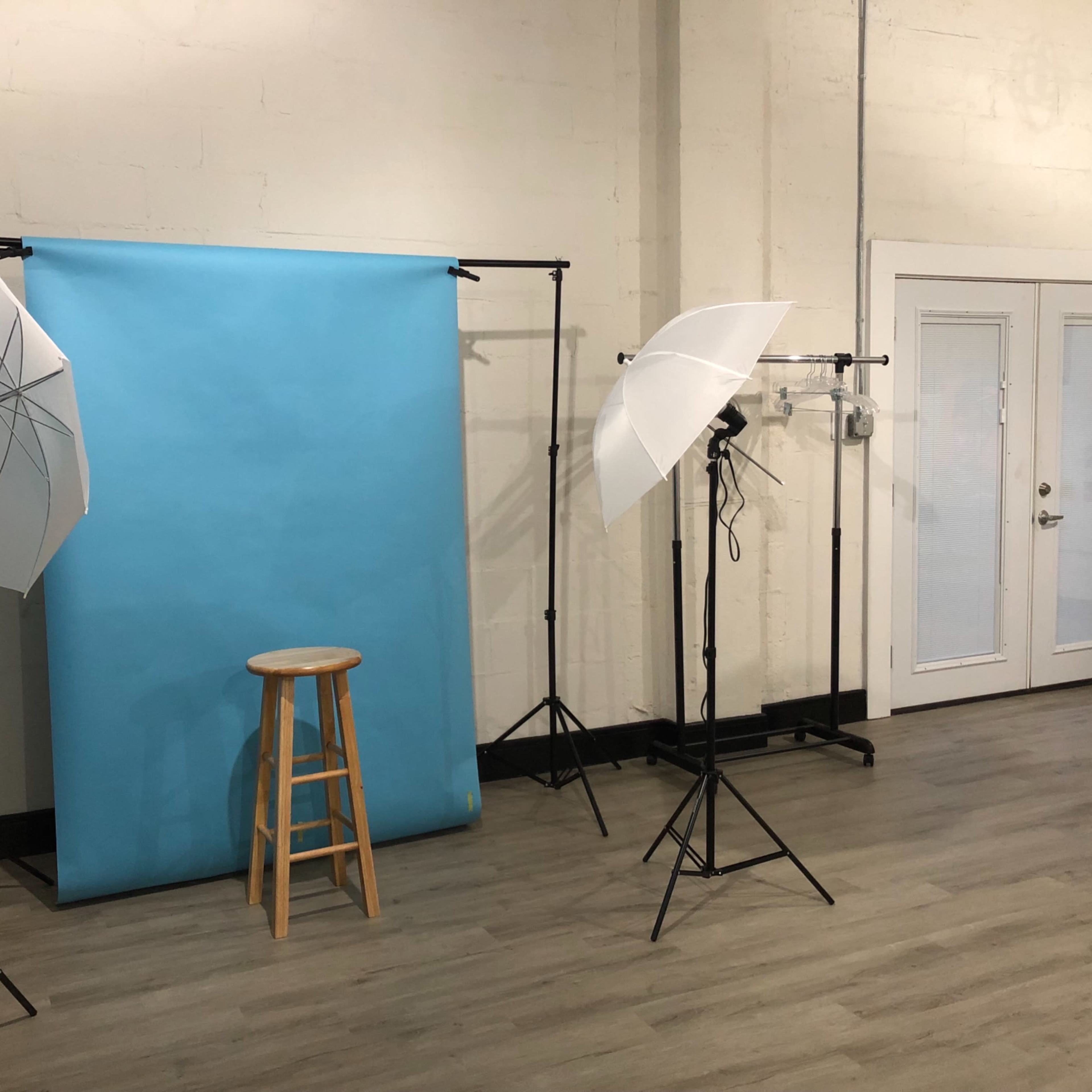 A photography setup with a blue backdrop, a wooden stool in front, and two softbox lights positioned on either side.