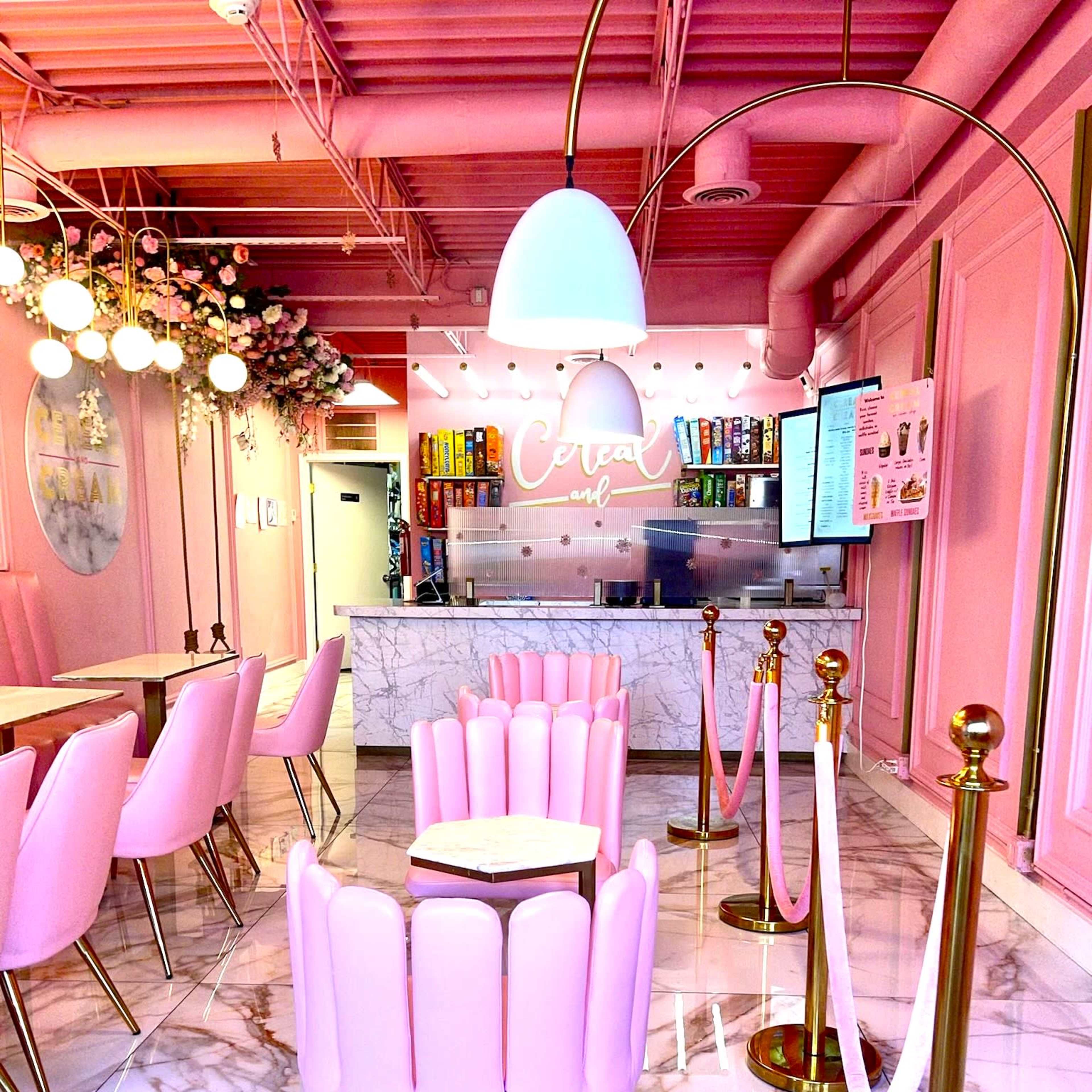 A vibrant café interior featuring pink chairs and walls, a marble counter with a menu display, and decorative lighting.