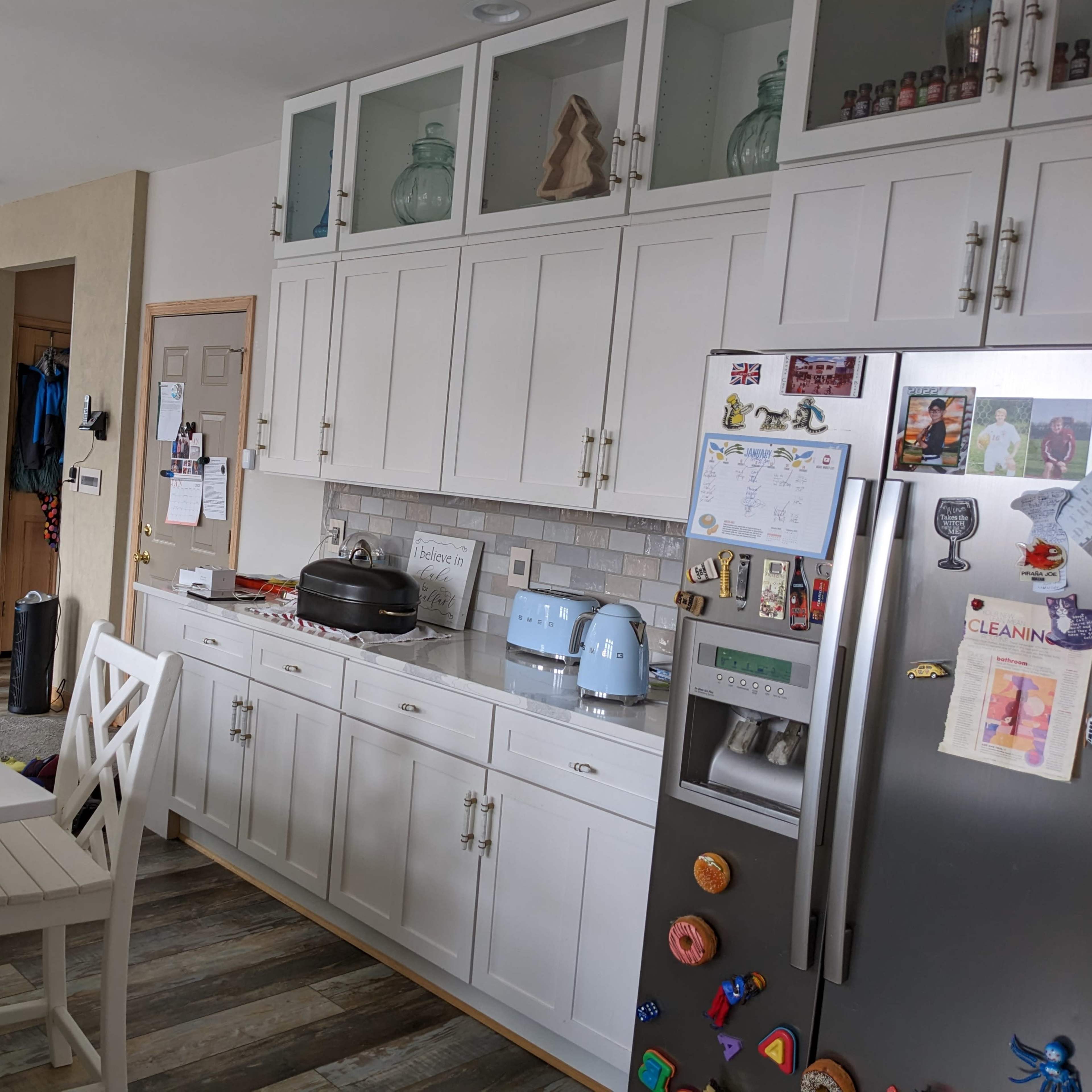 A modern kitchen features white cabinets, a stainless steel refrigerator, and a breakfast bar with light-colored stools.