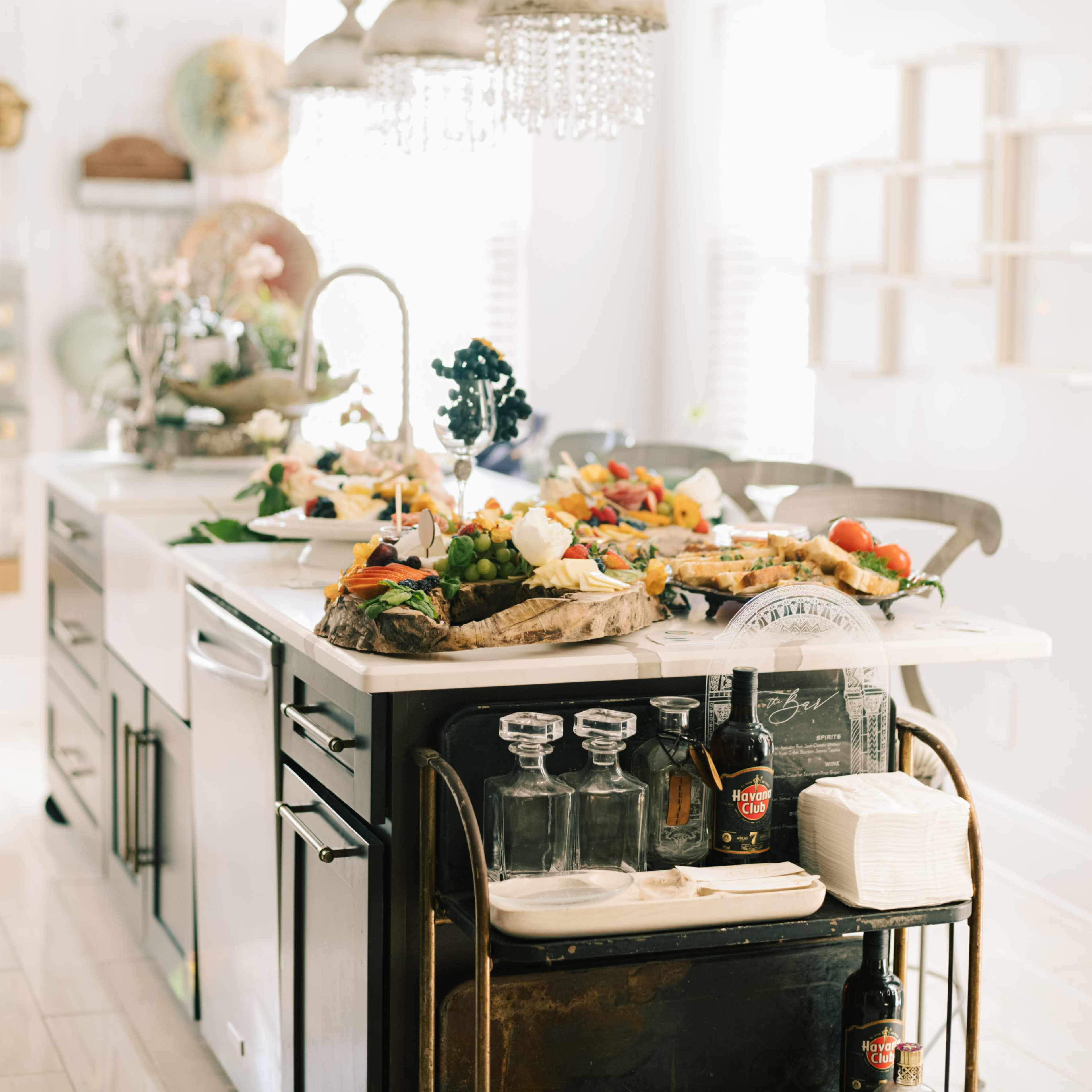 A modern kitchen island displays an array of colorful food items, surrounded by stylish lighting fixtures and equipped with various kitchen tools.
