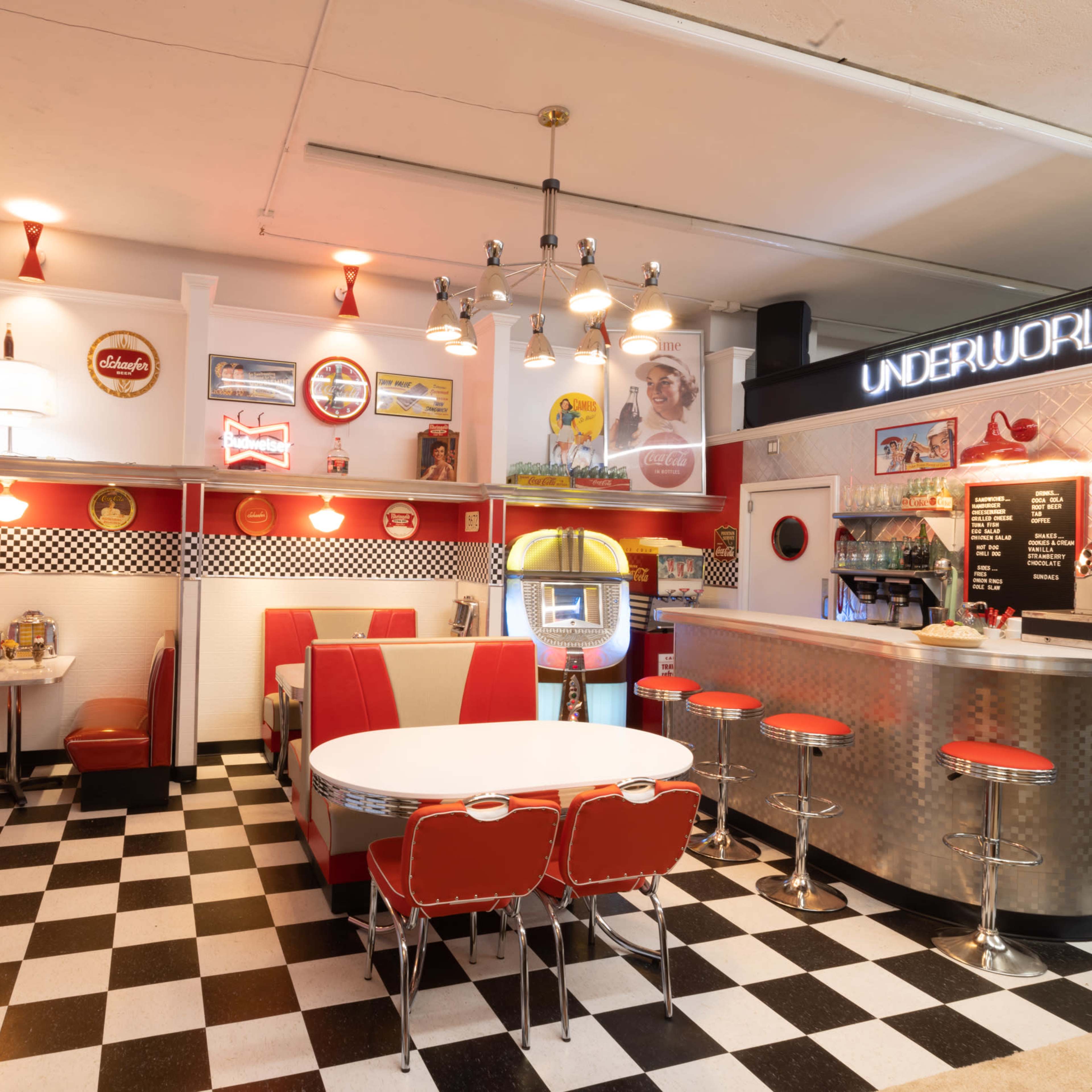 A vintage diner with a checkered black-and-white floor, red and white booths, a counter with stools, and retro decorations.
