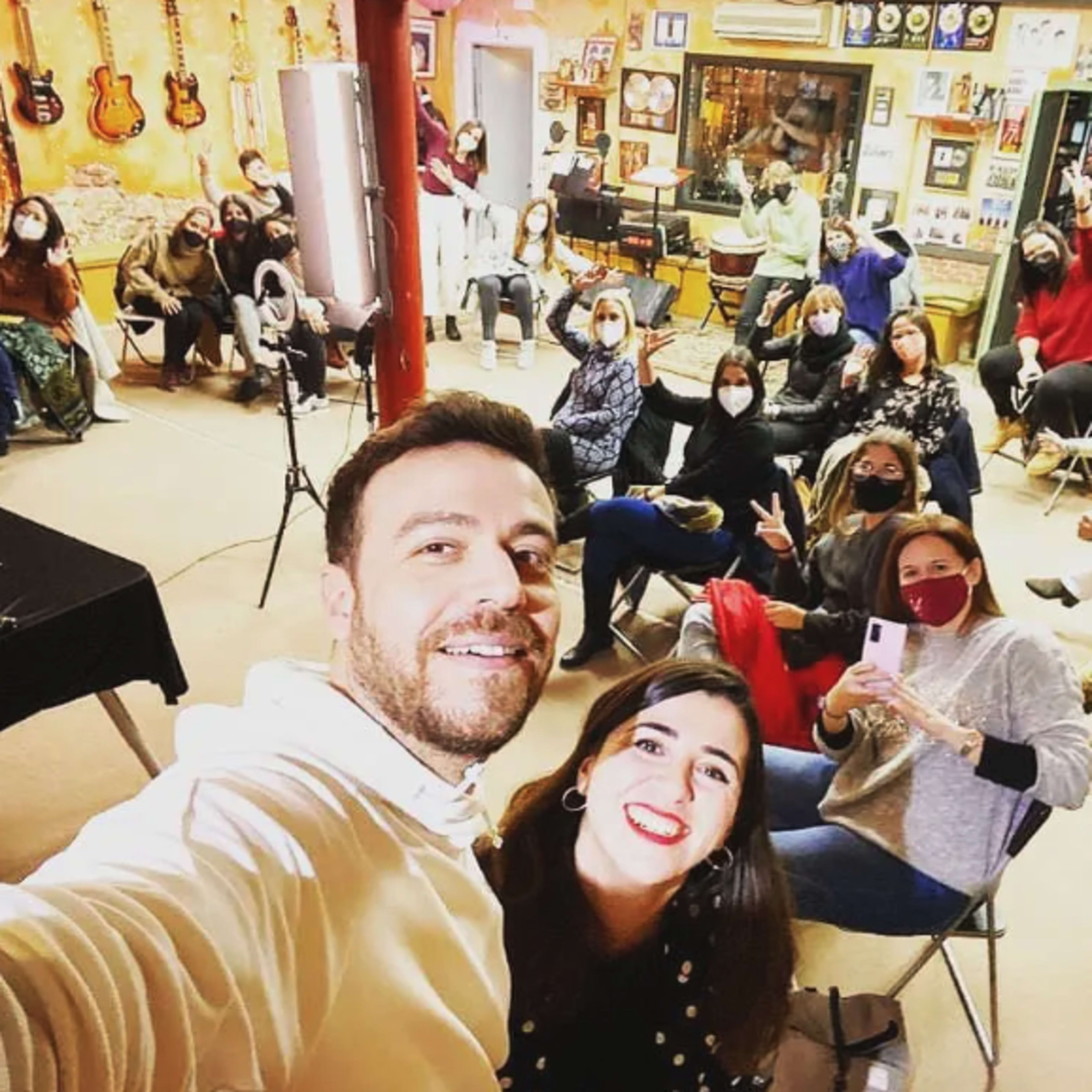 A group of people wearing masks gathers in a music studio with guitars and various decorations on the walls.
