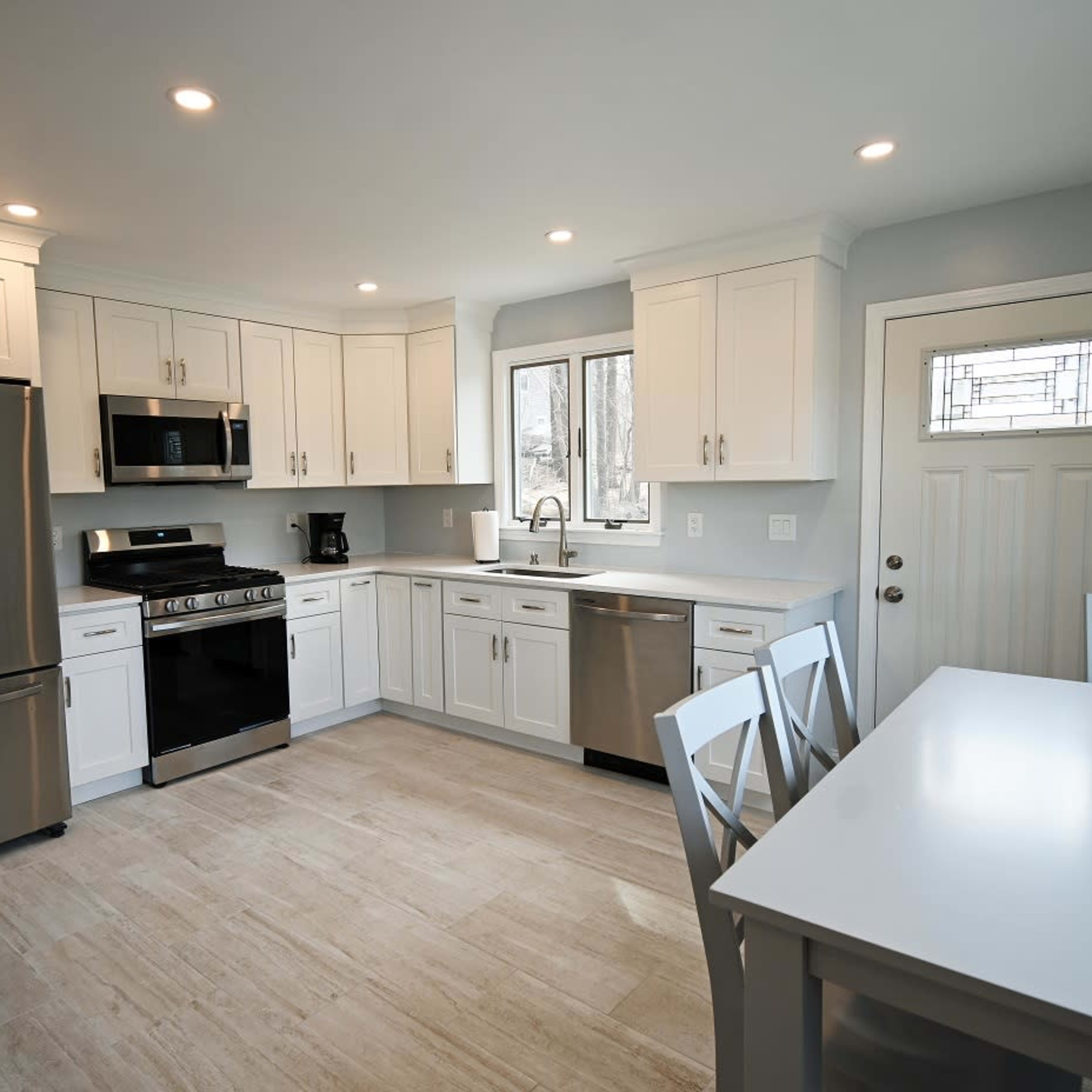 The kitchen features white cabinetry, stainless steel appliances, and a dining table with four chairs.