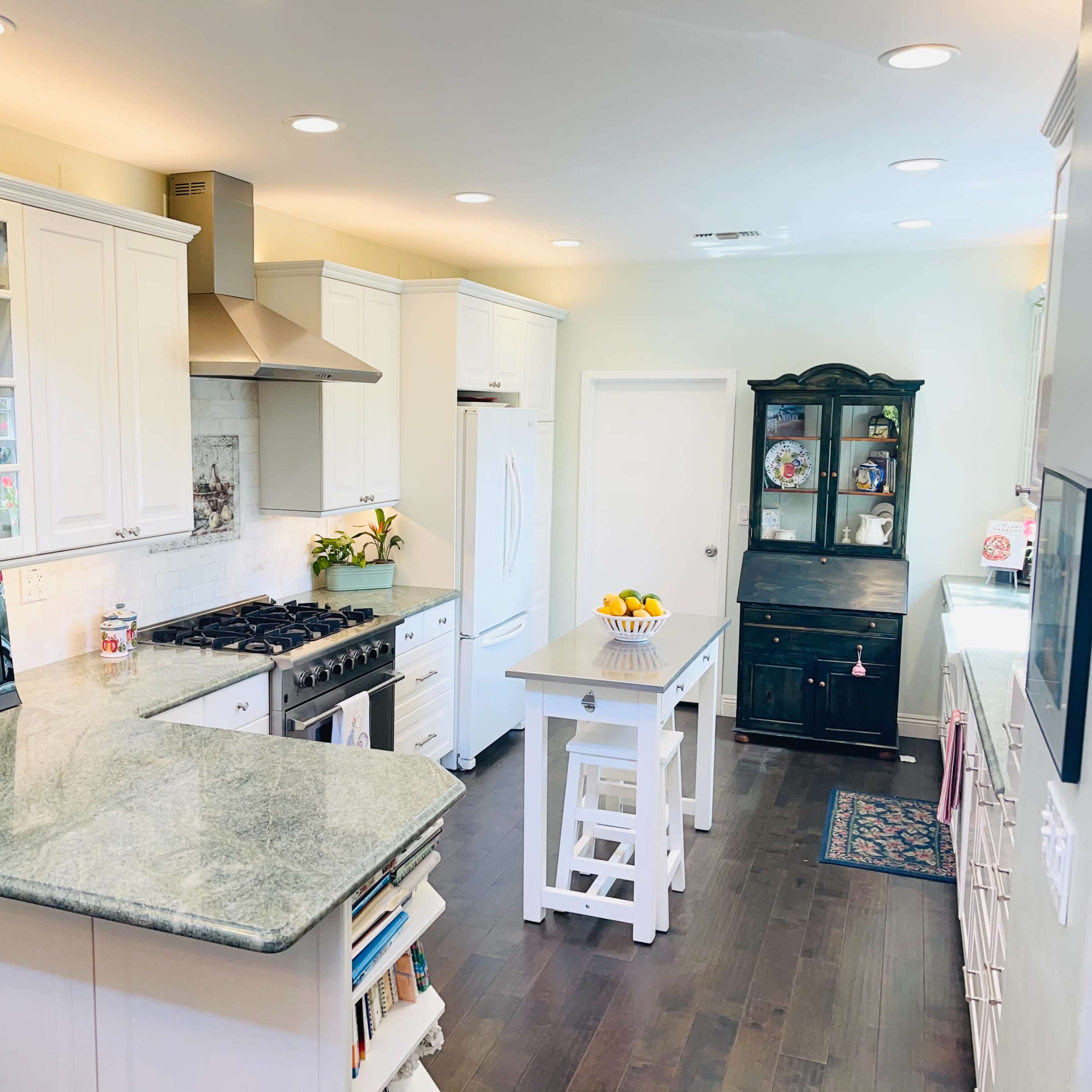 A modern kitchen featuring white cabinets, a large green stone countertop, a gas stove, and a dark wooden dining table on one side.