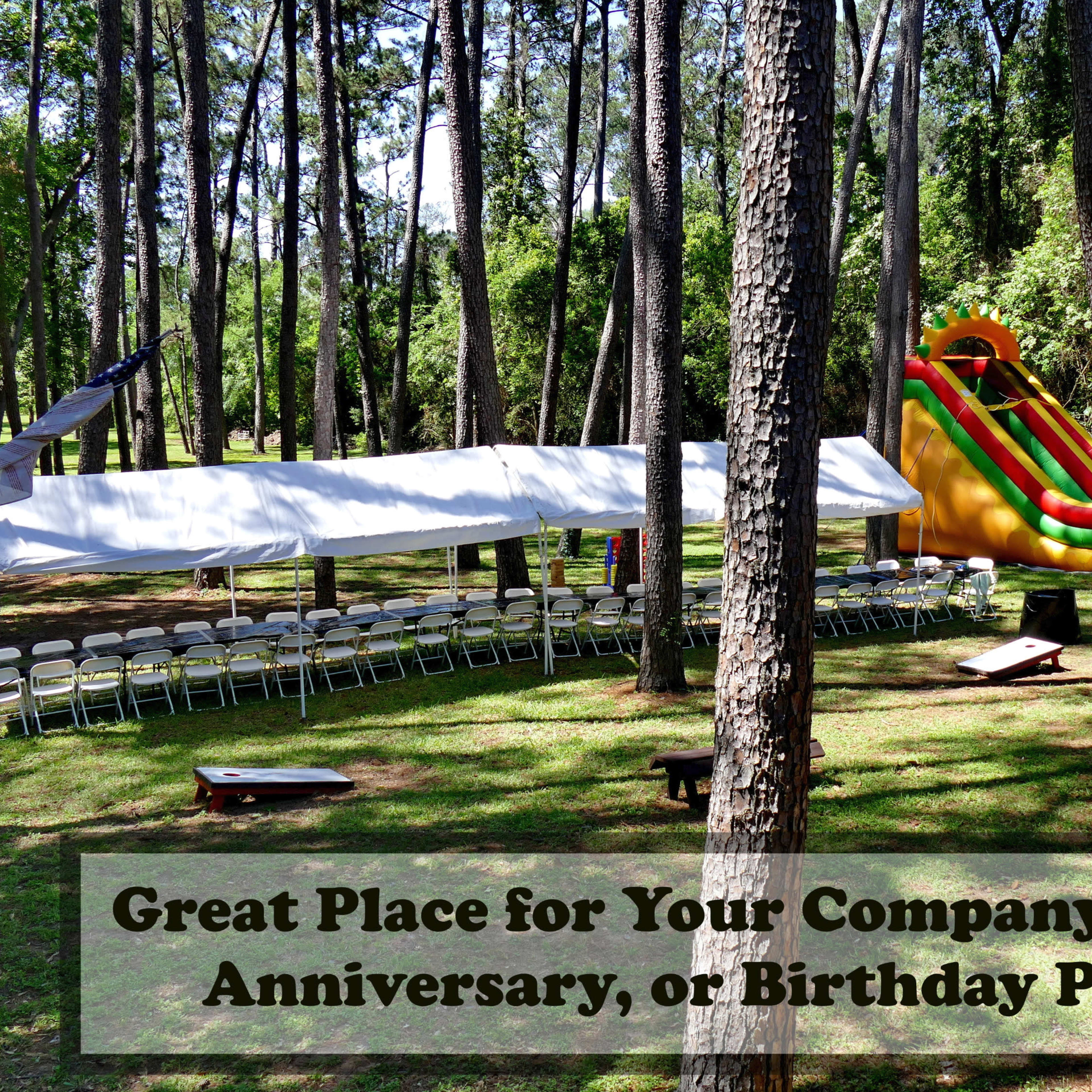 A tent with rows of chairs is set up in a wooded area alongside a colorful inflatable slide.