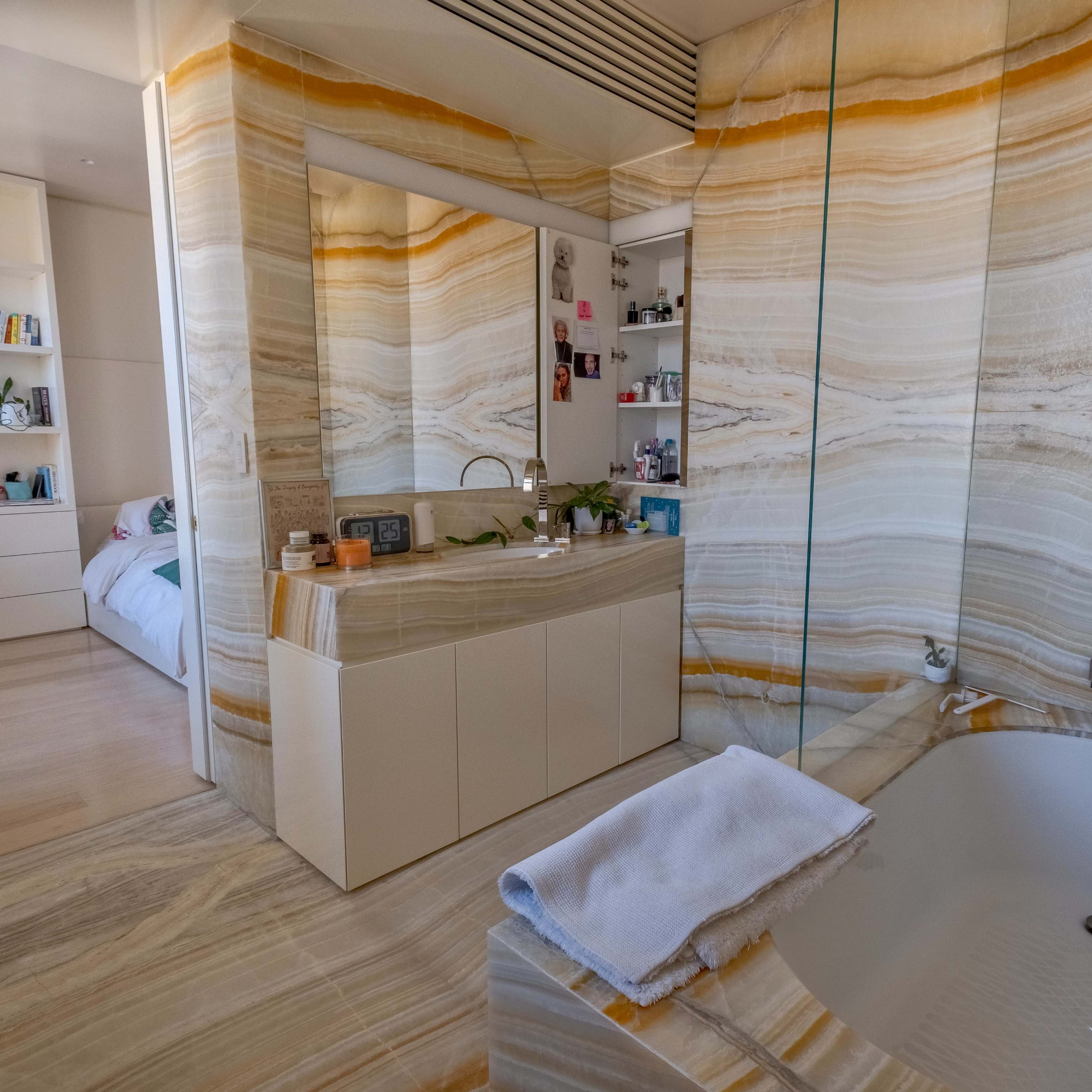 A modern bathroom featuring a large, curved soaking tub, a vanity with a mirror, and walls adorned with striking marble patterns.
