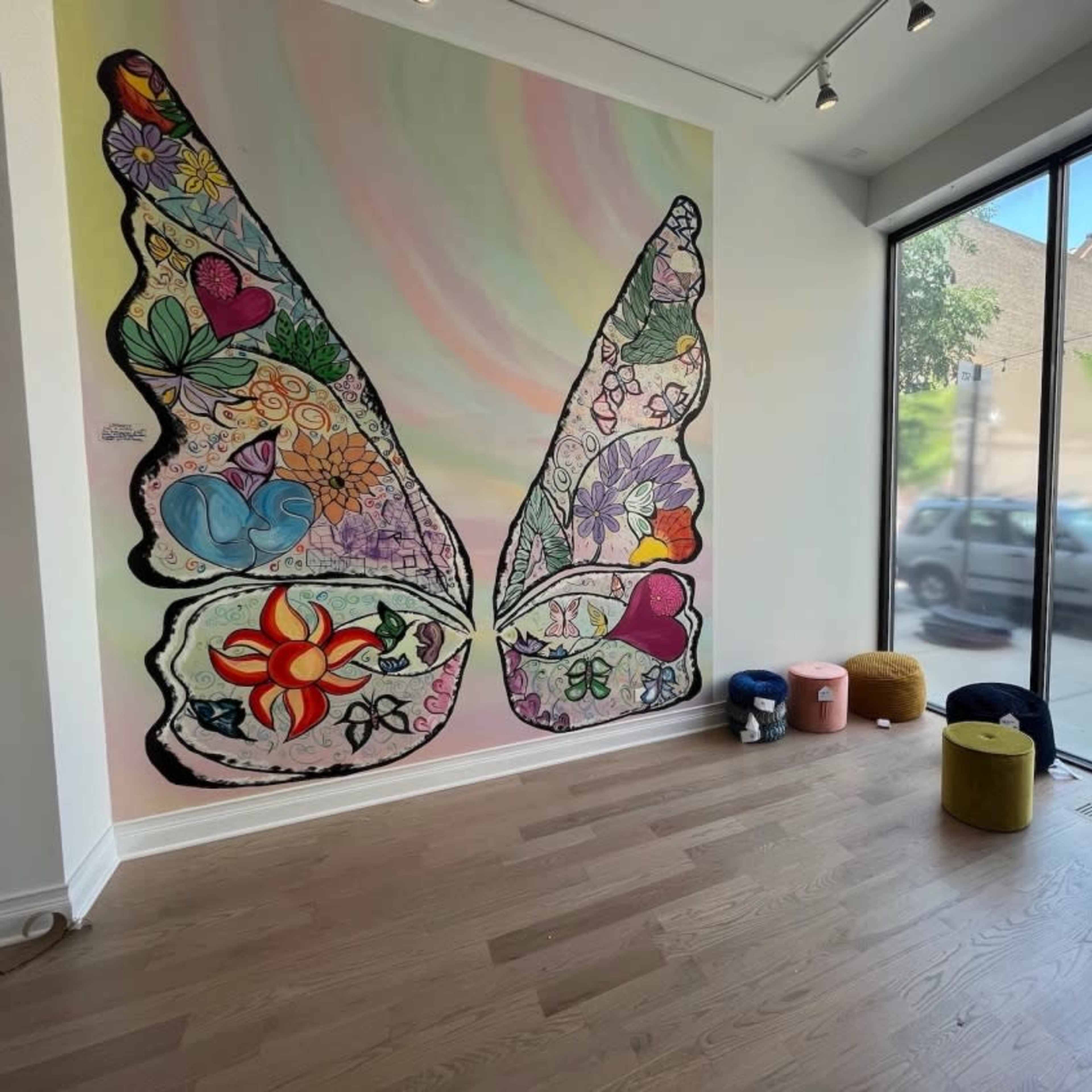 A spacious room featuring a large butterfly mural on the wall and several colorful stools arranged on the floor.
