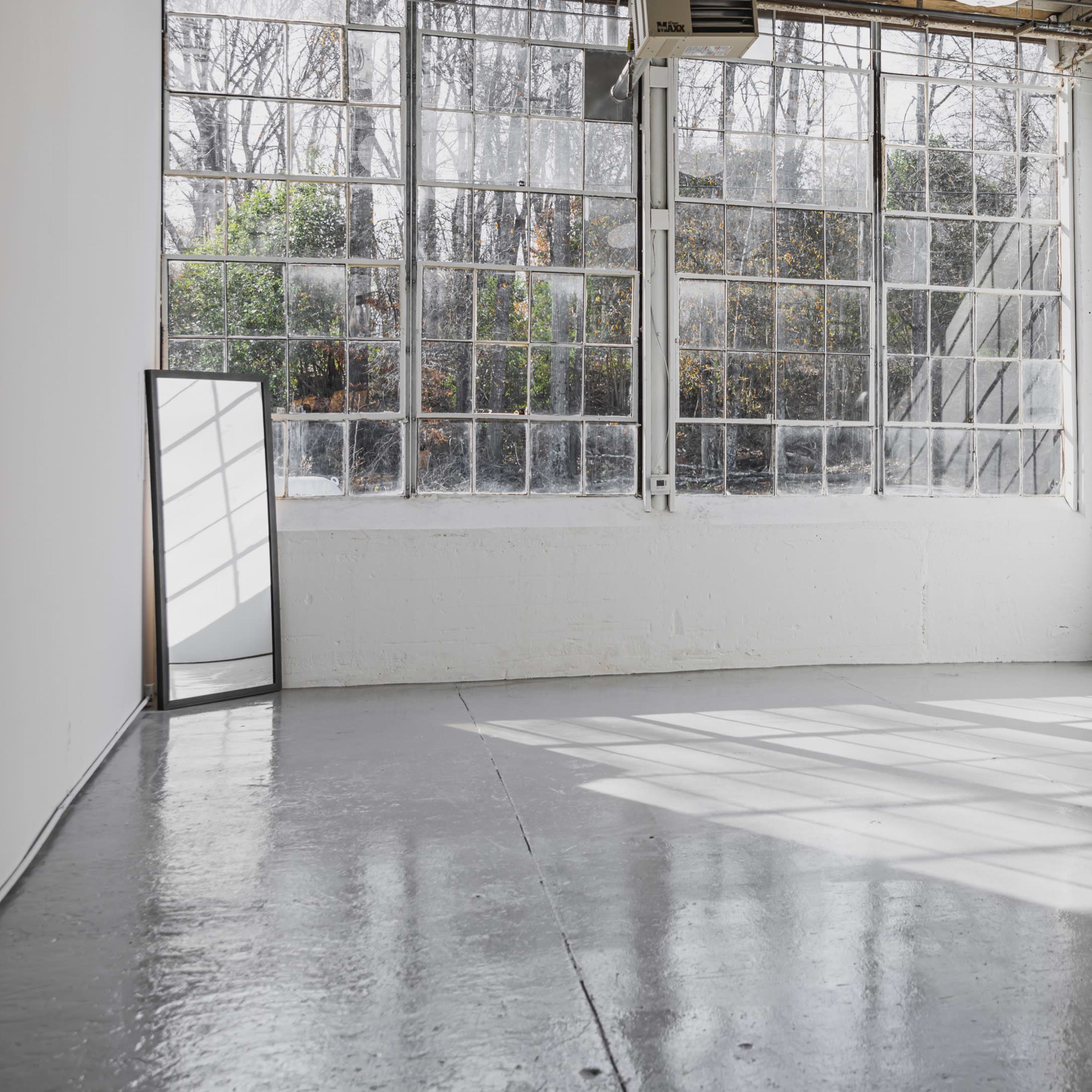 A spacious, empty room with large windows allowing sunlight to cast shadows on the polished concrete floor.