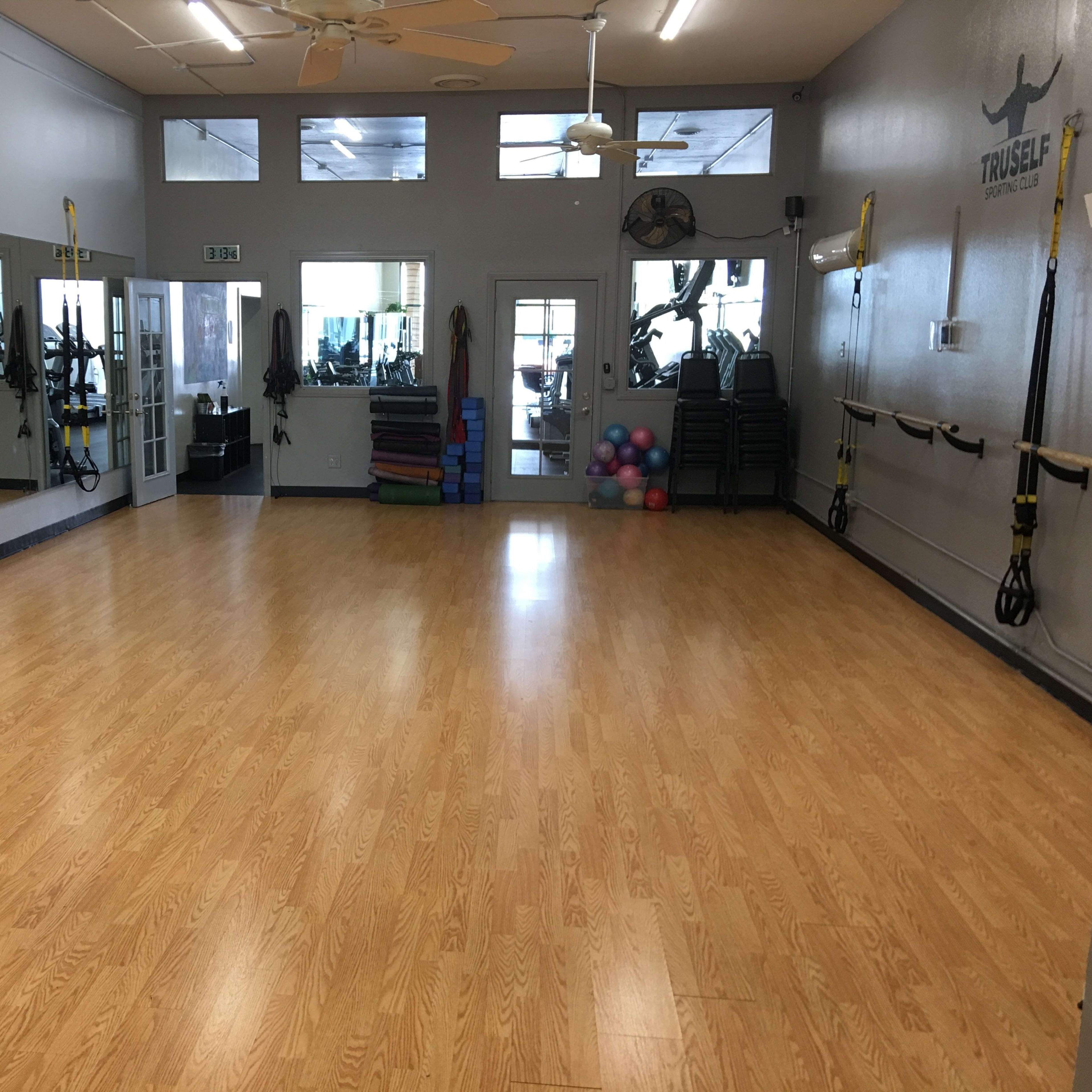 A spacious exercise studio with a wooden floor, large mirrors, and various fitness equipment along the walls.
