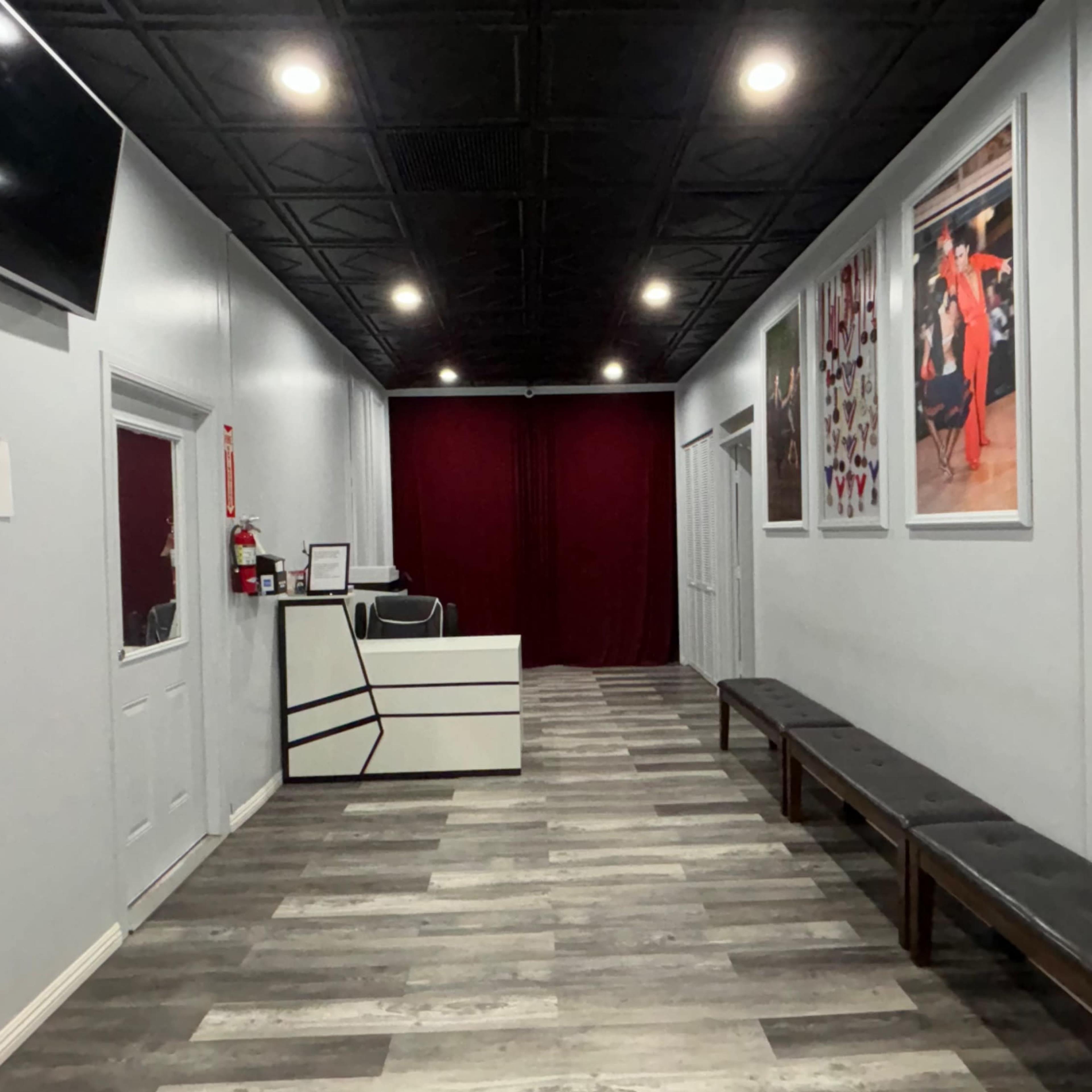 A long, narrow hallway with a reception area at the end, featuring gray walls, wooden flooring, and benches along the sides.
