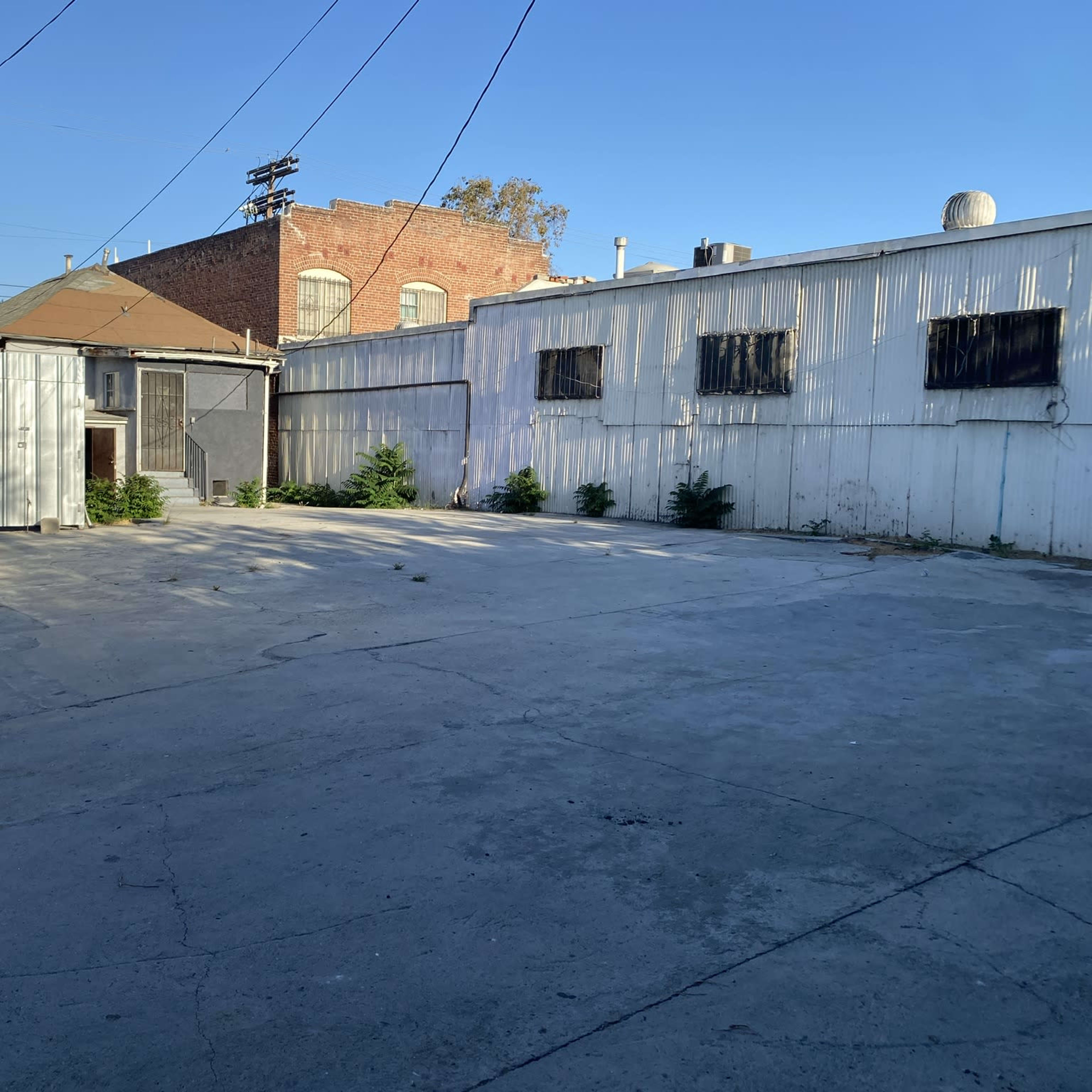 An empty concrete lot surrounded by metal and brick buildings under a clear blue sky.
