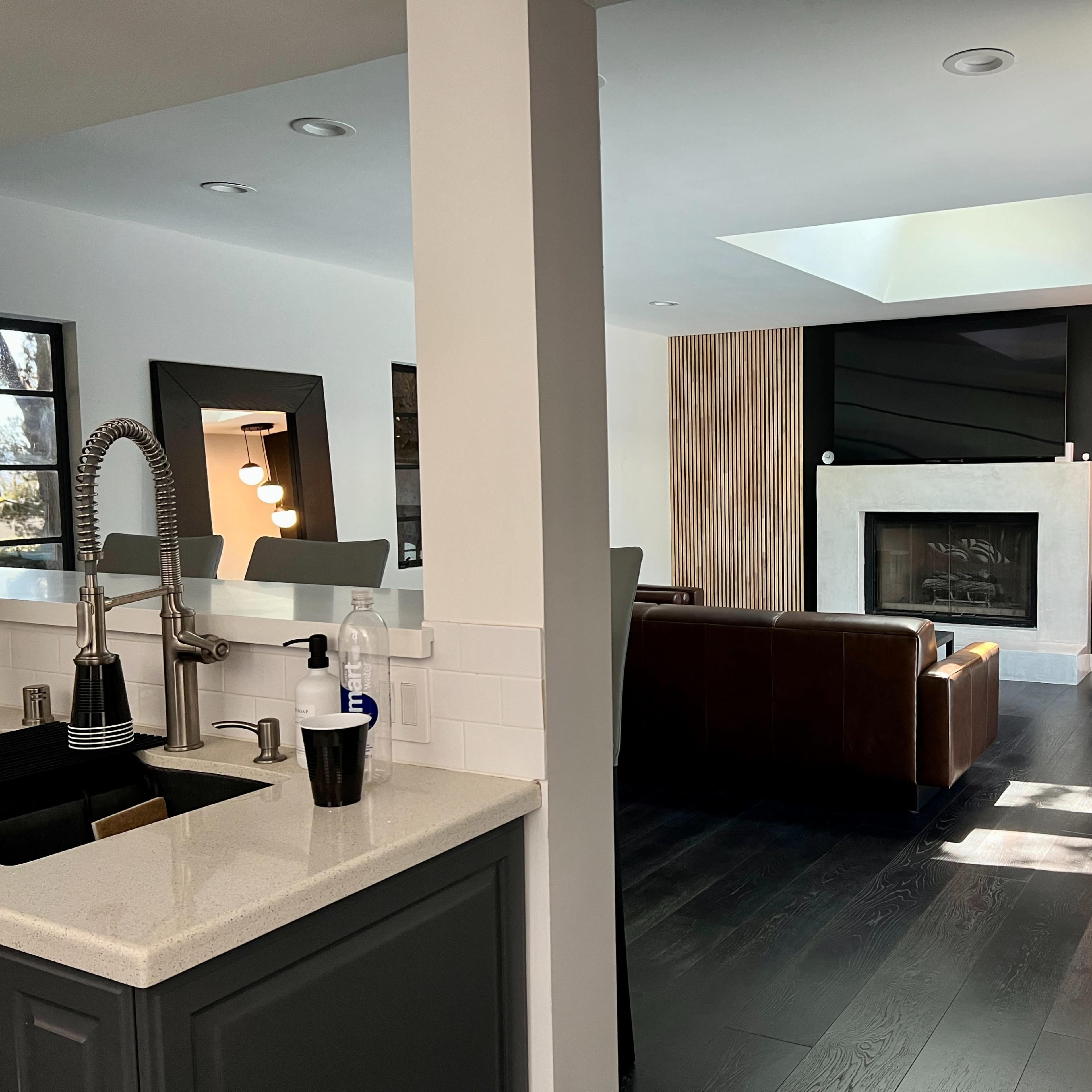 A modern living room with a fireplace and a seating area, viewed from a kitchen with a sink.