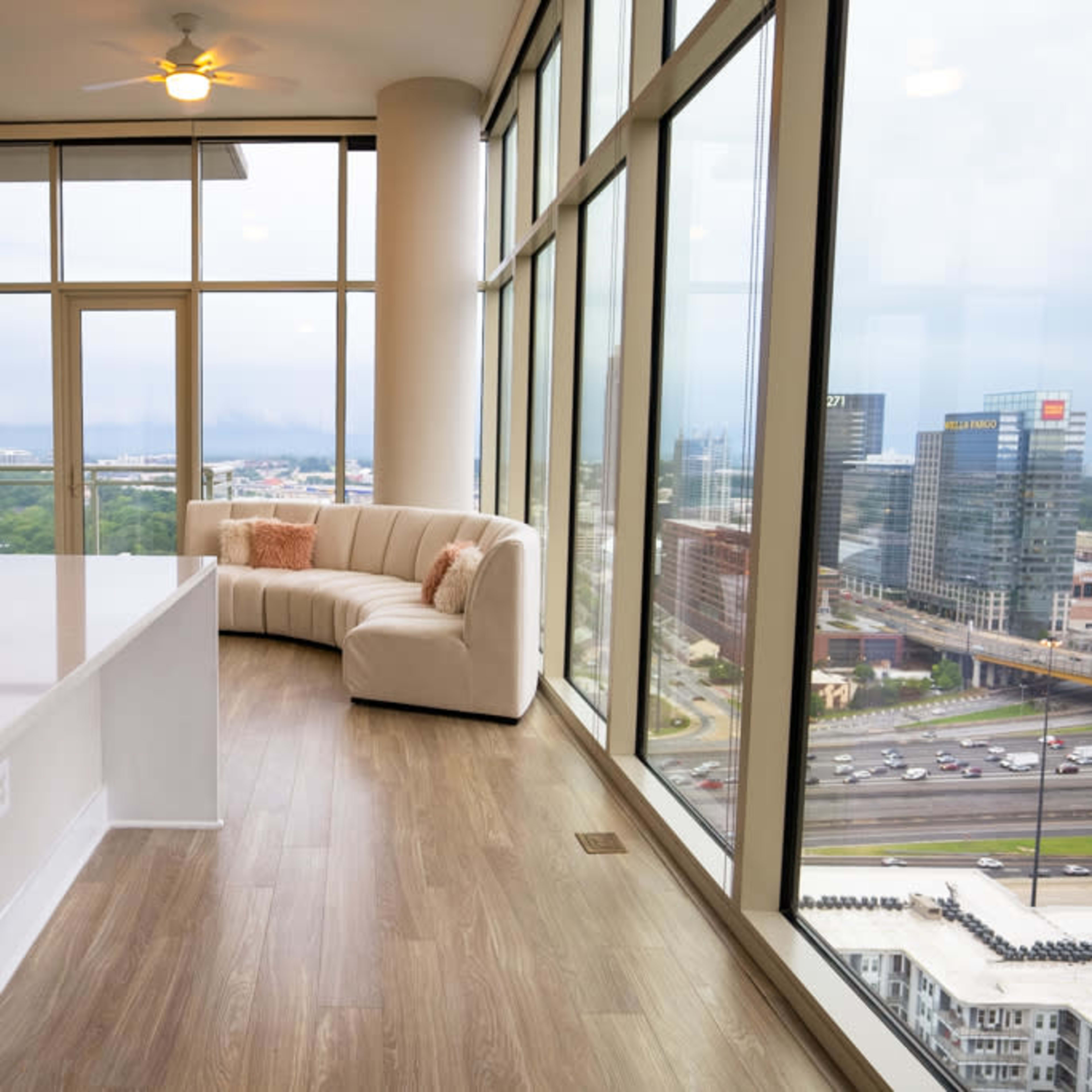 A modern apartment interior with a curved white couch and large floor-to-ceiling windows overlooking a cityscape.