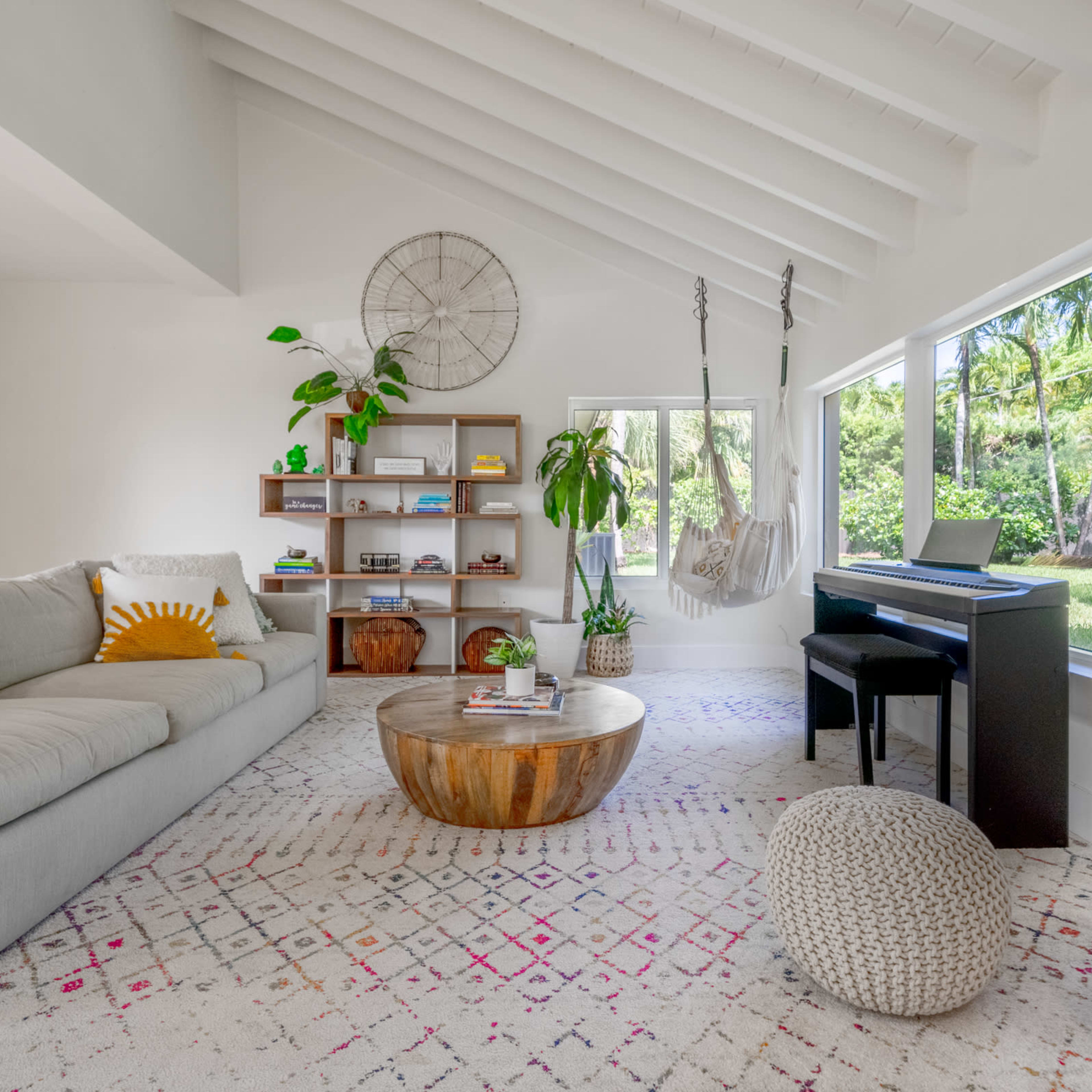 The living room features a light gray sofa, a wooden coffee table, a black piano, and large windows that reveal a view of a garden with a basketball hoop.