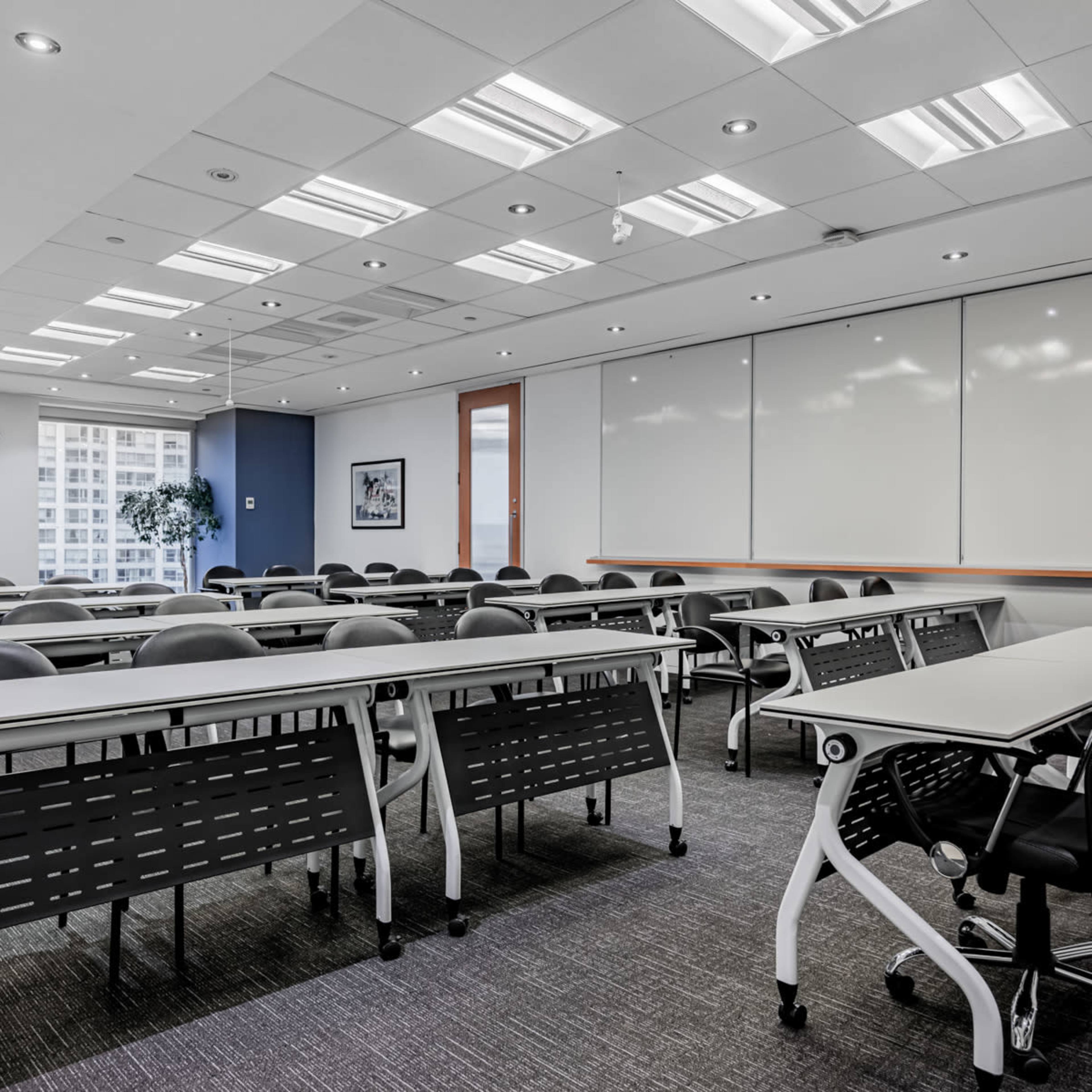A modern conference room features rows of tables and chairs, large windows, and a whiteboard wall.