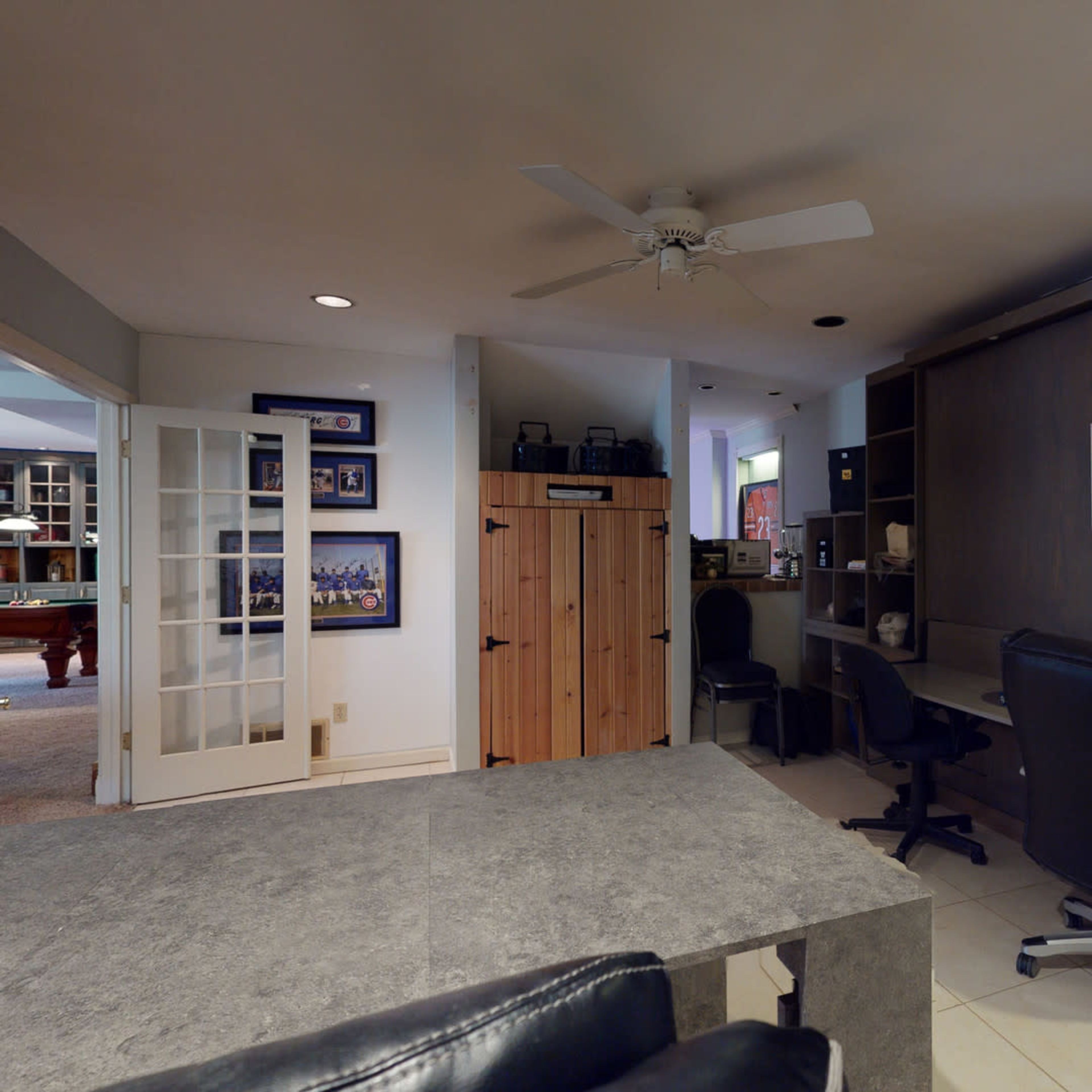 A home office space featuring a large desk, two office chairs, and a storage cabinet, with a door leading to another room visible in the background.