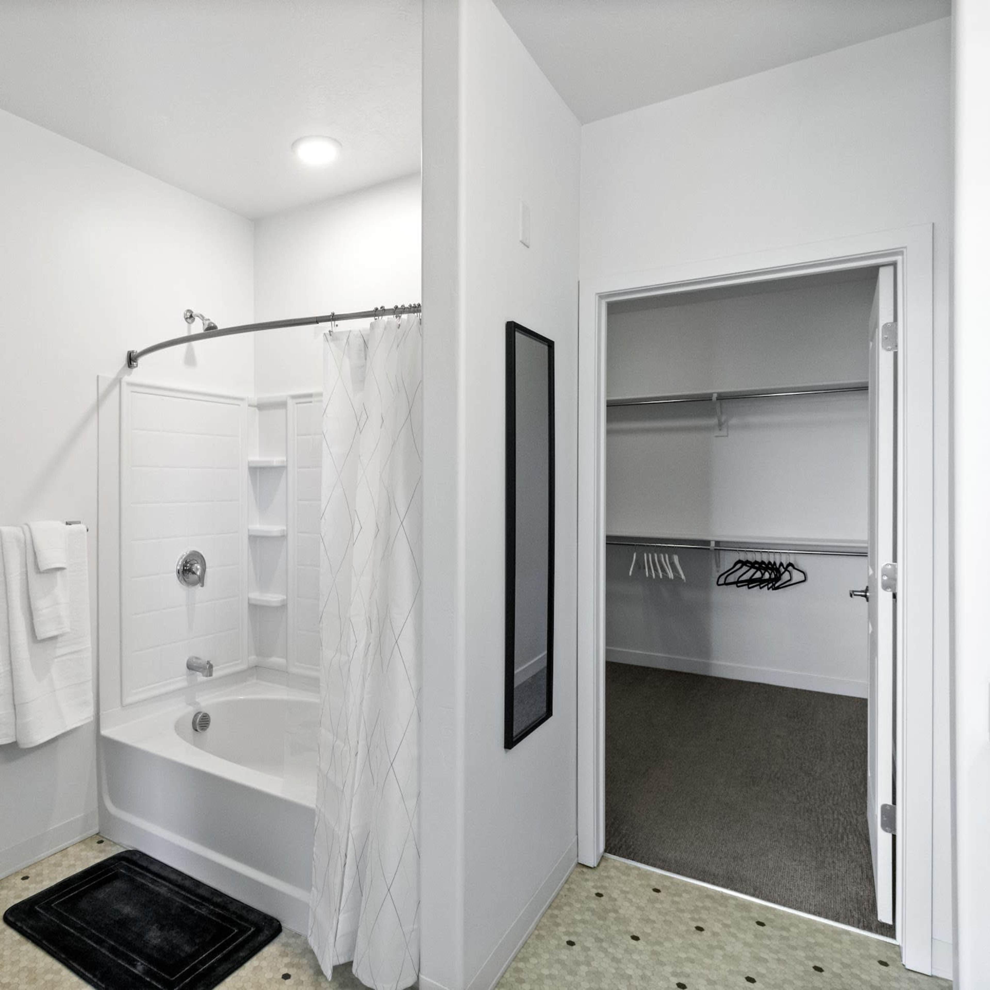 A clean bathroom featuring a shower with a curved curtain rod, hanging towels, a toilet, and a closet with empty hangers.
