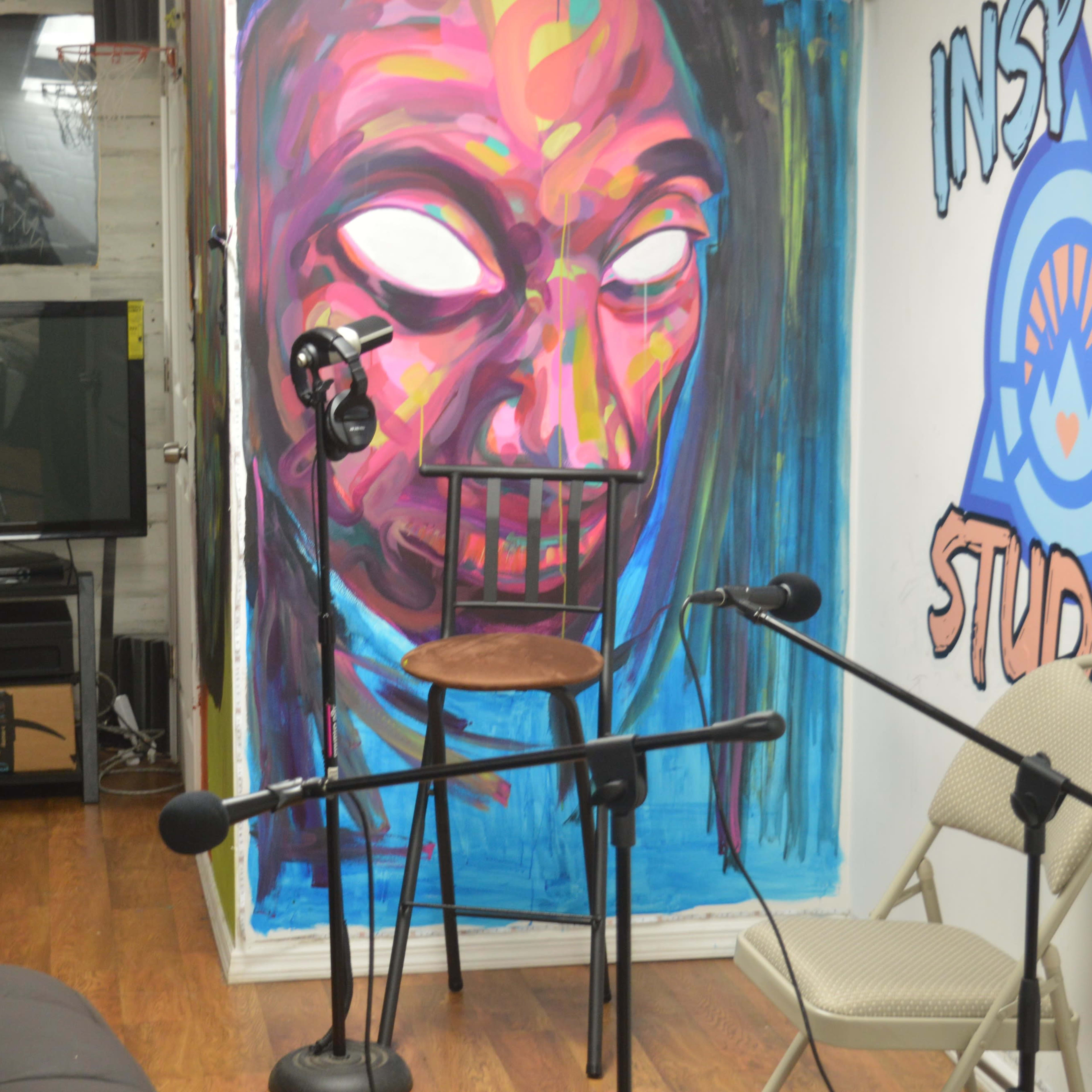 A studio space with a large mural featuring a face, a chair, and microphones arranged around the area.