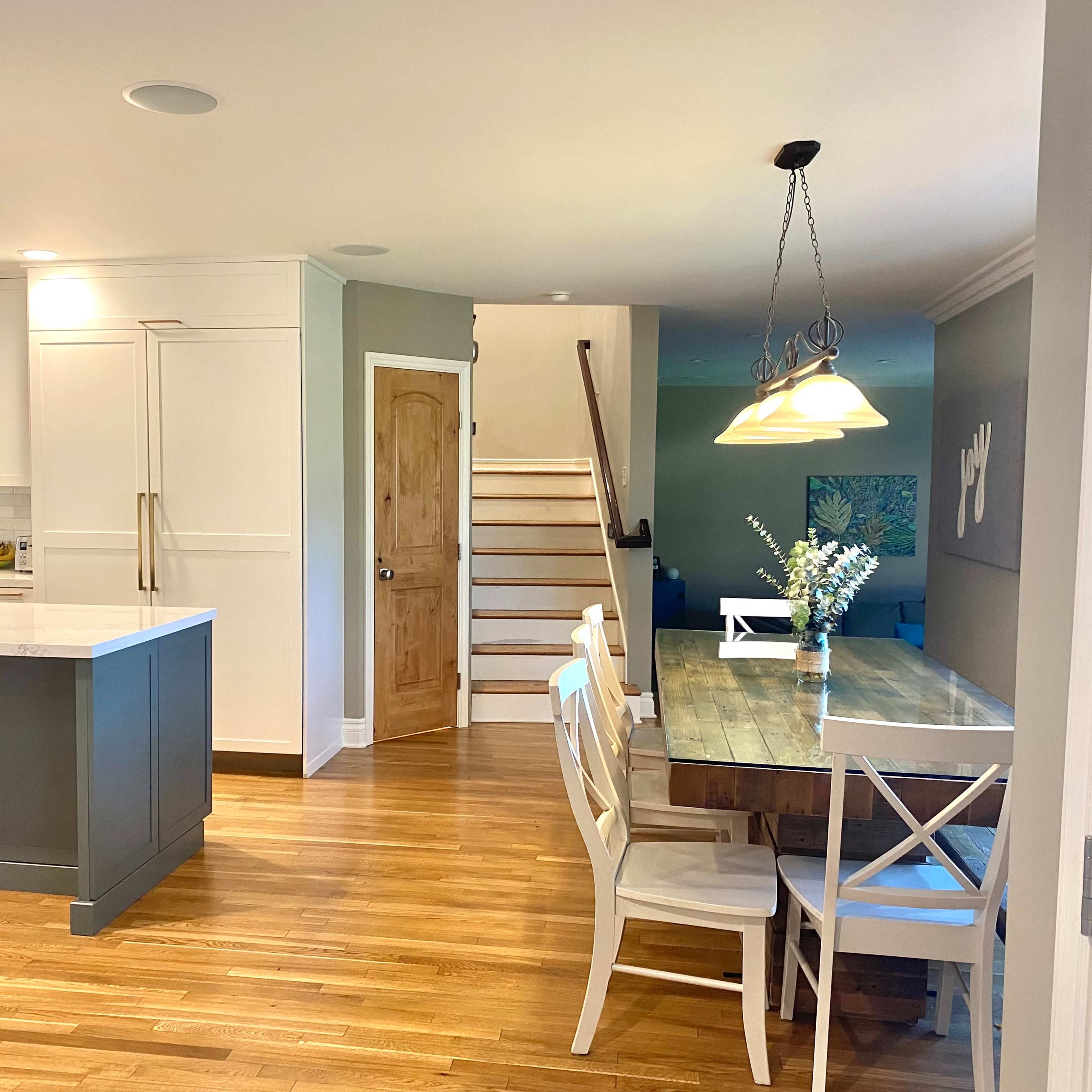 A modern kitchen and dining area with a wooden table, white chairs, and an open staircase in the background.