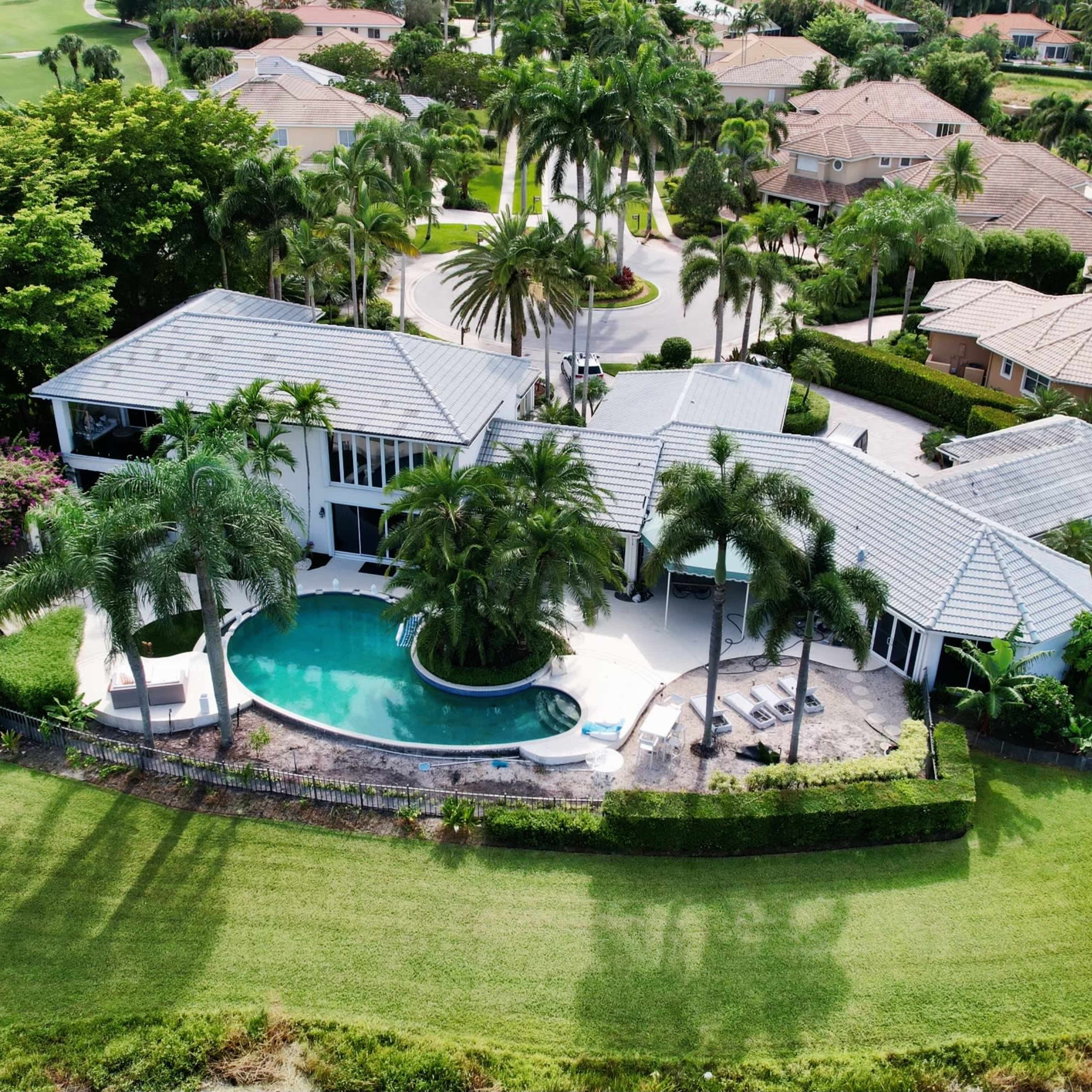 A modern home with a pool, surrounded by manicured landscaping and palm trees in a residential neighborhood.