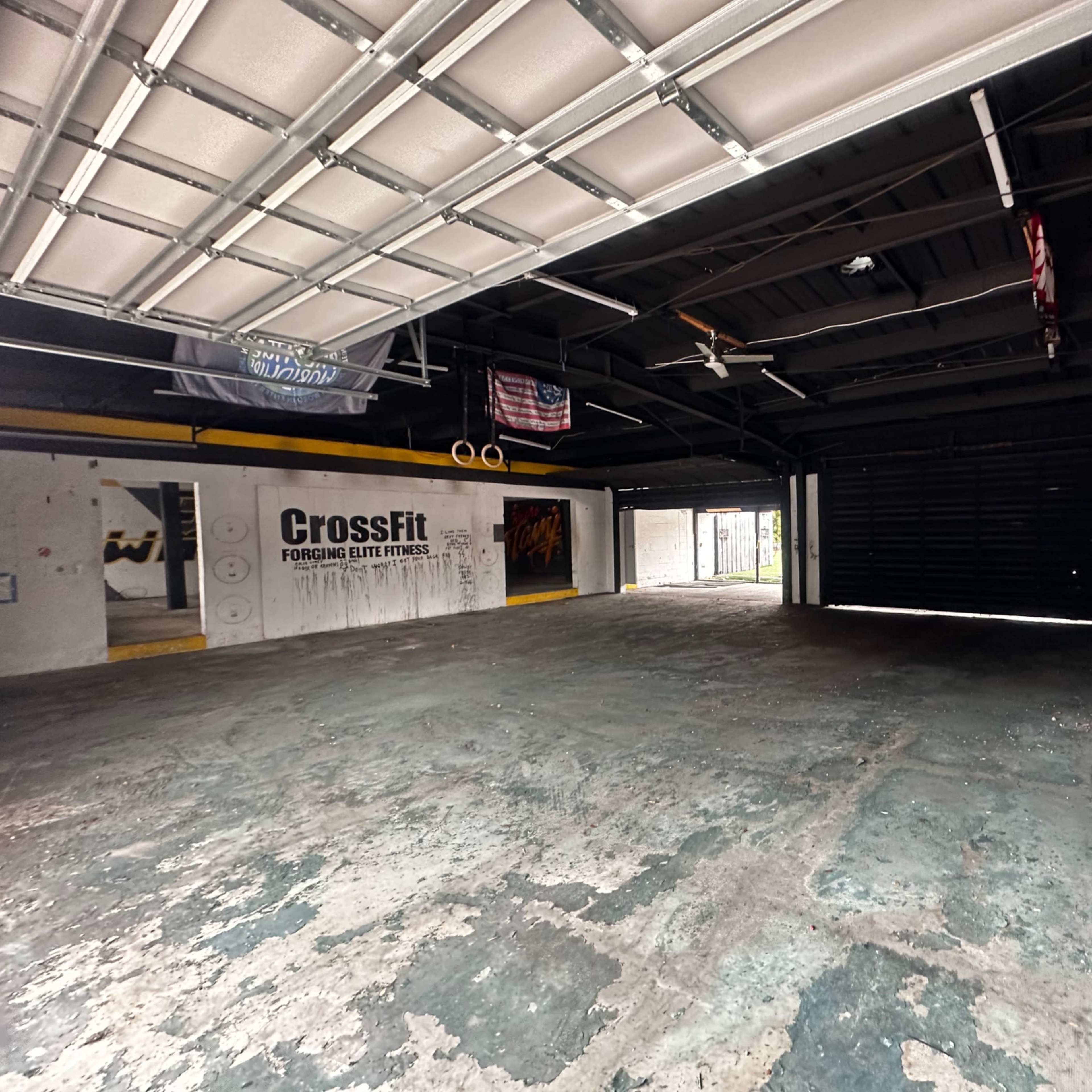 An empty CrossFit gym with a concrete floor and large, open garage doors.