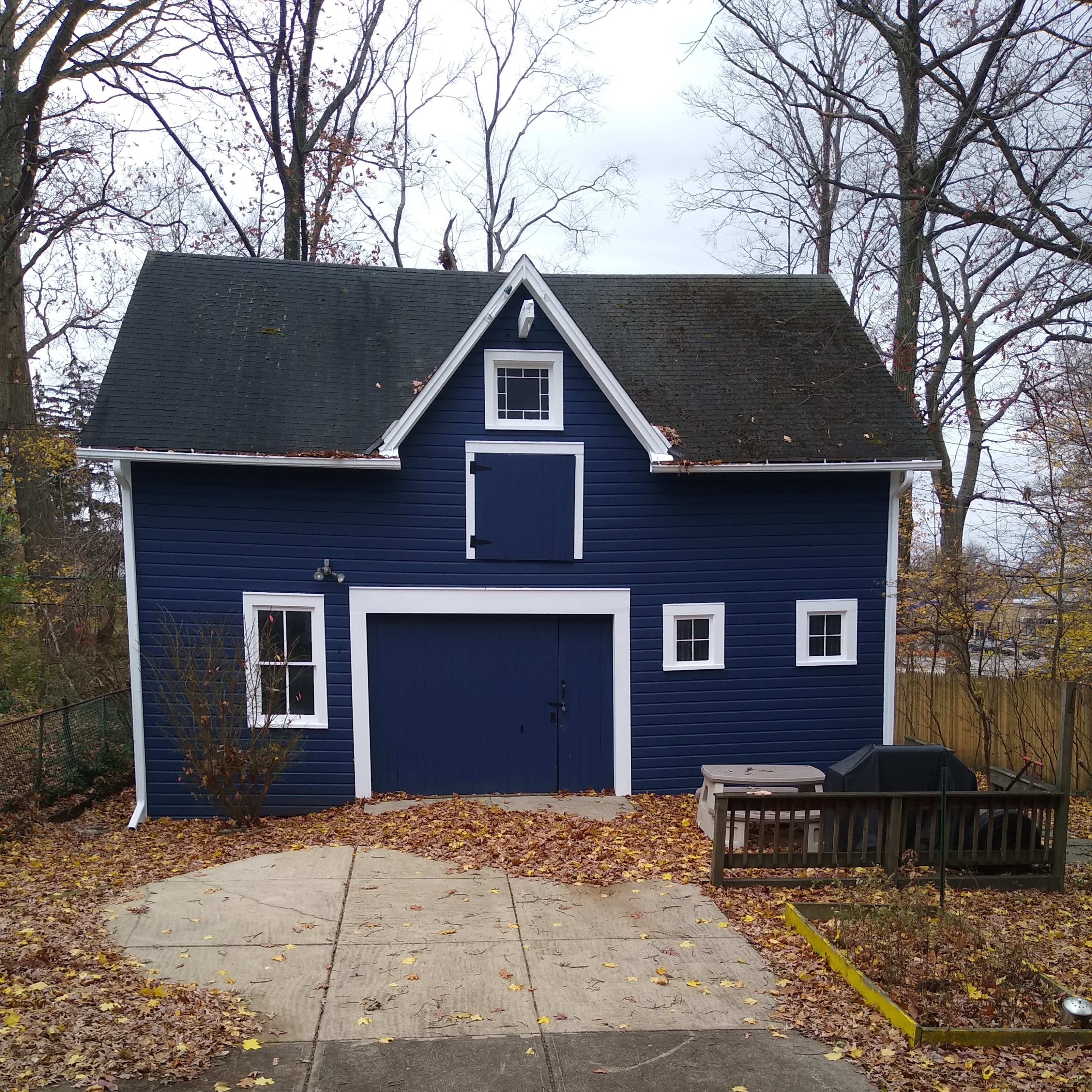 A blue barn-style shed surrounded by fallen leaves and a concrete driveway.