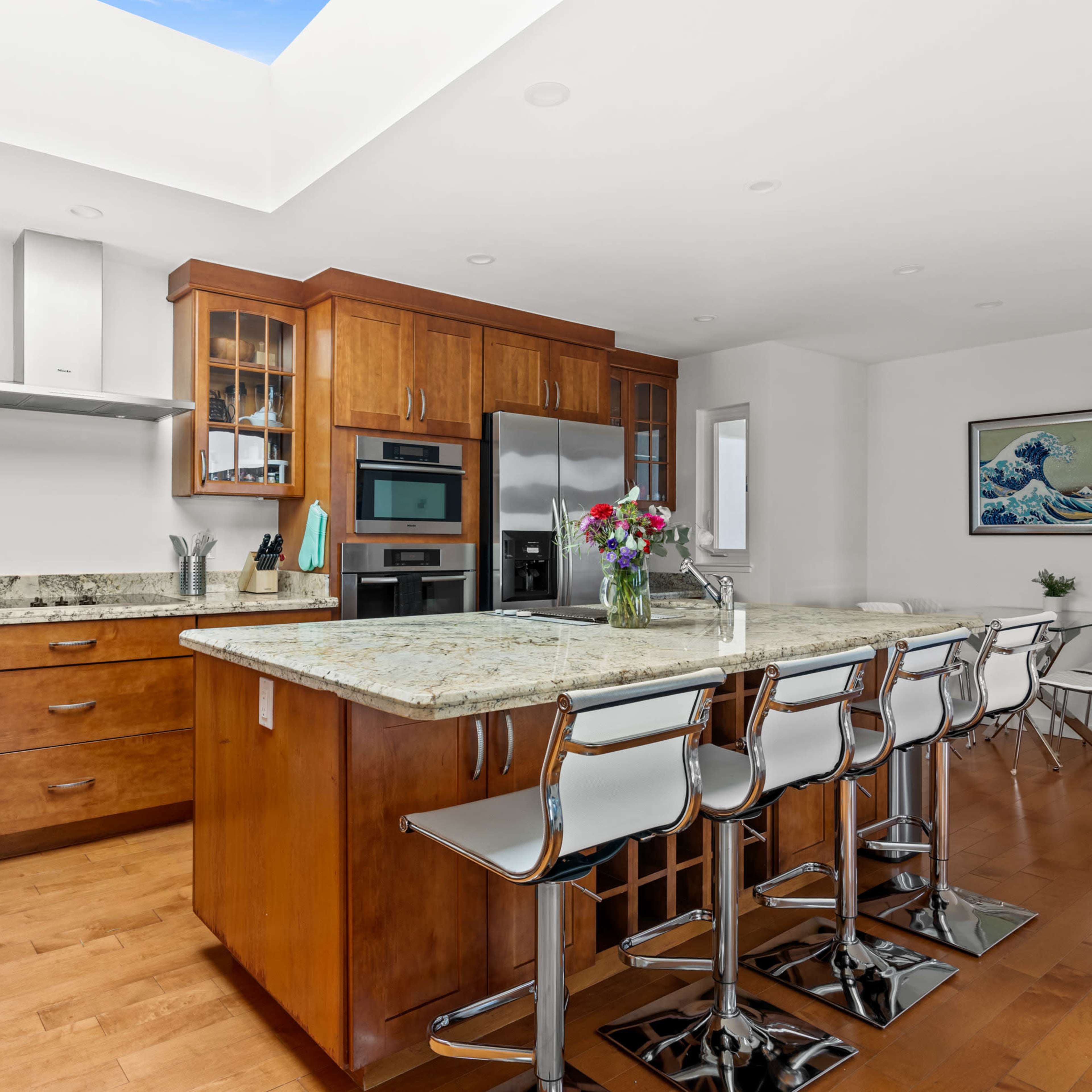 A modern kitchen with wooden cabinetry, a large island with bar stools, and abundant natural light coming from a skylight.