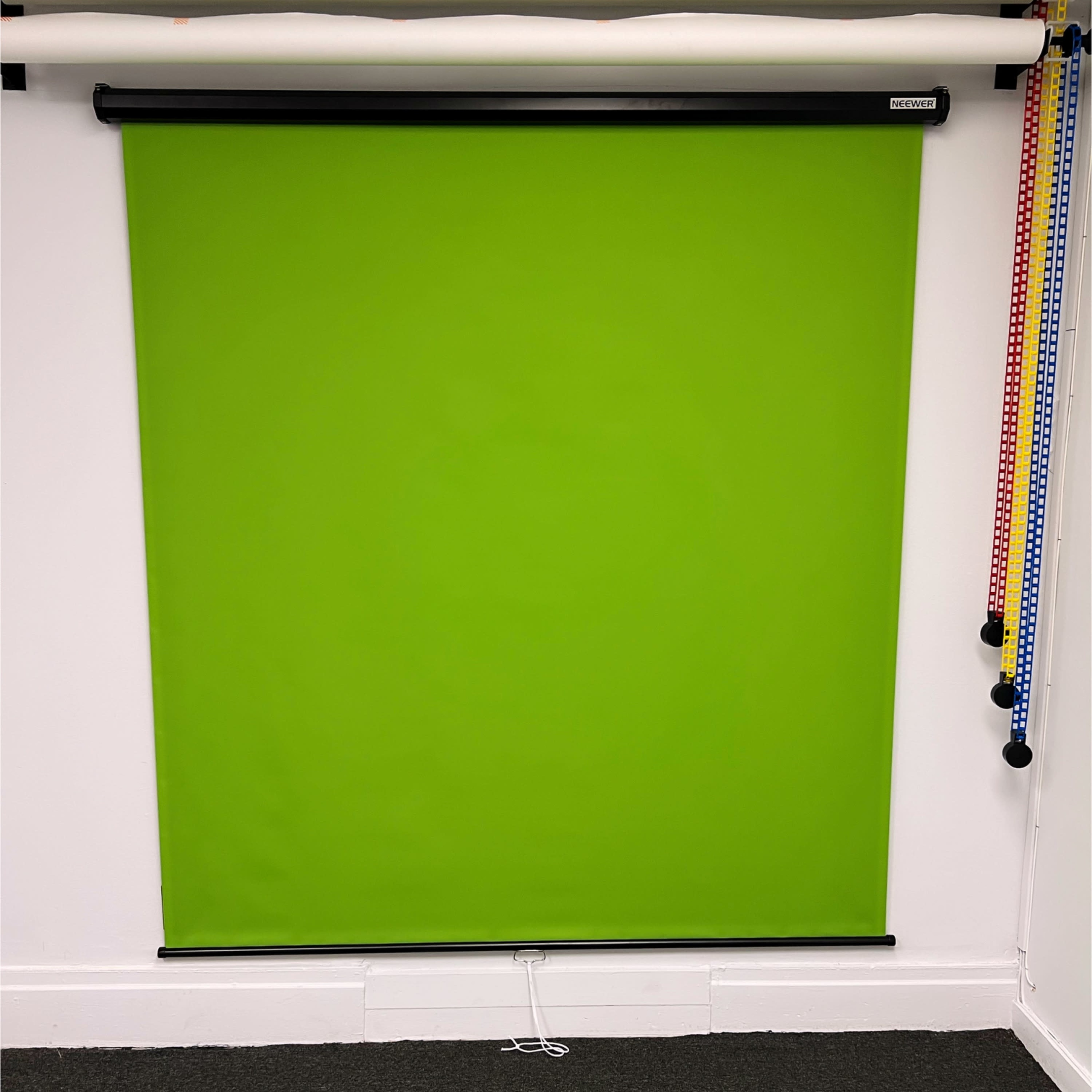 A green backdrop hanging from a black roller above a carpeted floor in a well-lit room.