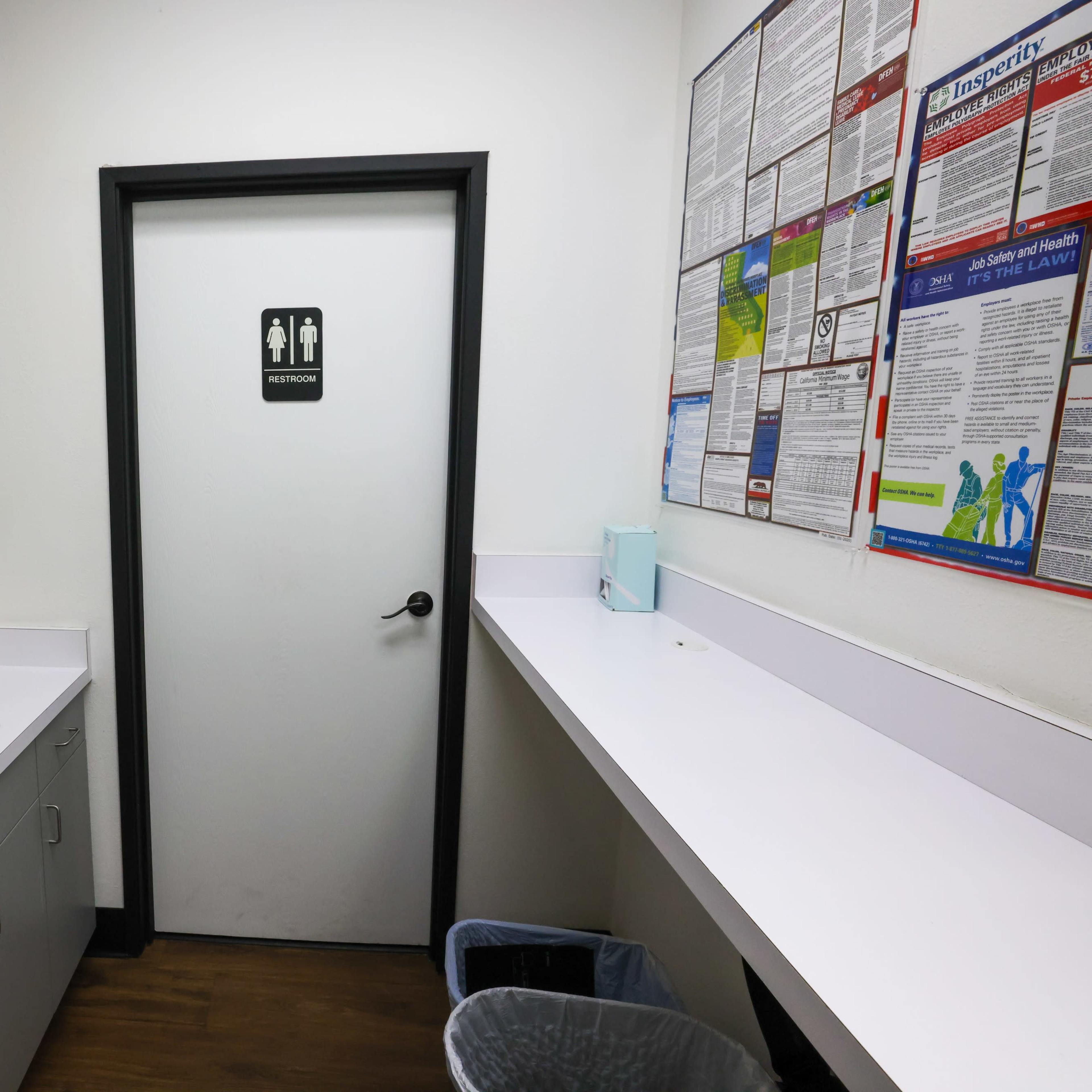 A small utility room with a sink, a paper towel dispenser, and a door labeled "RESTROOM," along with a bulletin board on the wall.