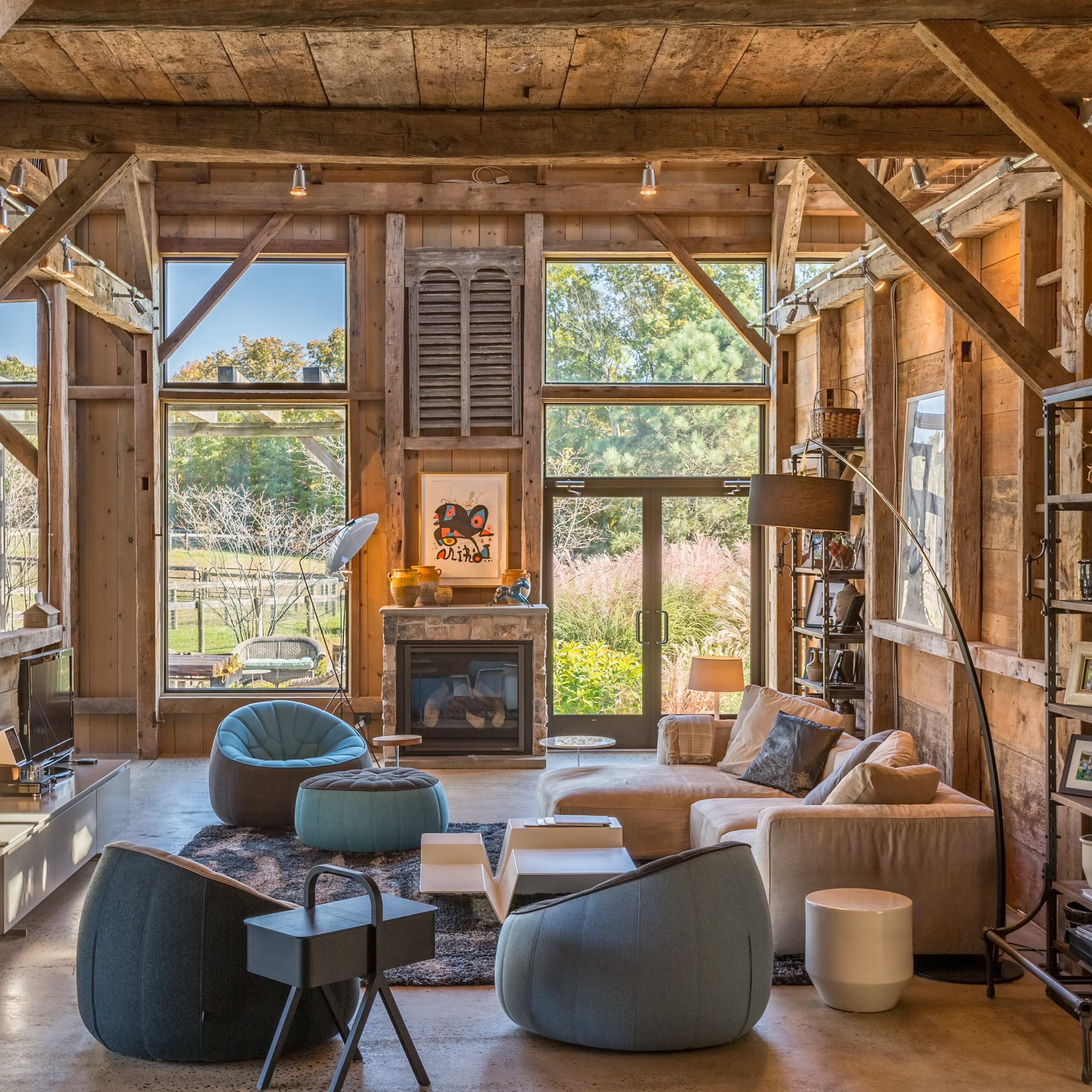 A spacious, rustic living room with exposed wooden beams, large windows, and a mix of modern and comfortable furniture arrangements.
