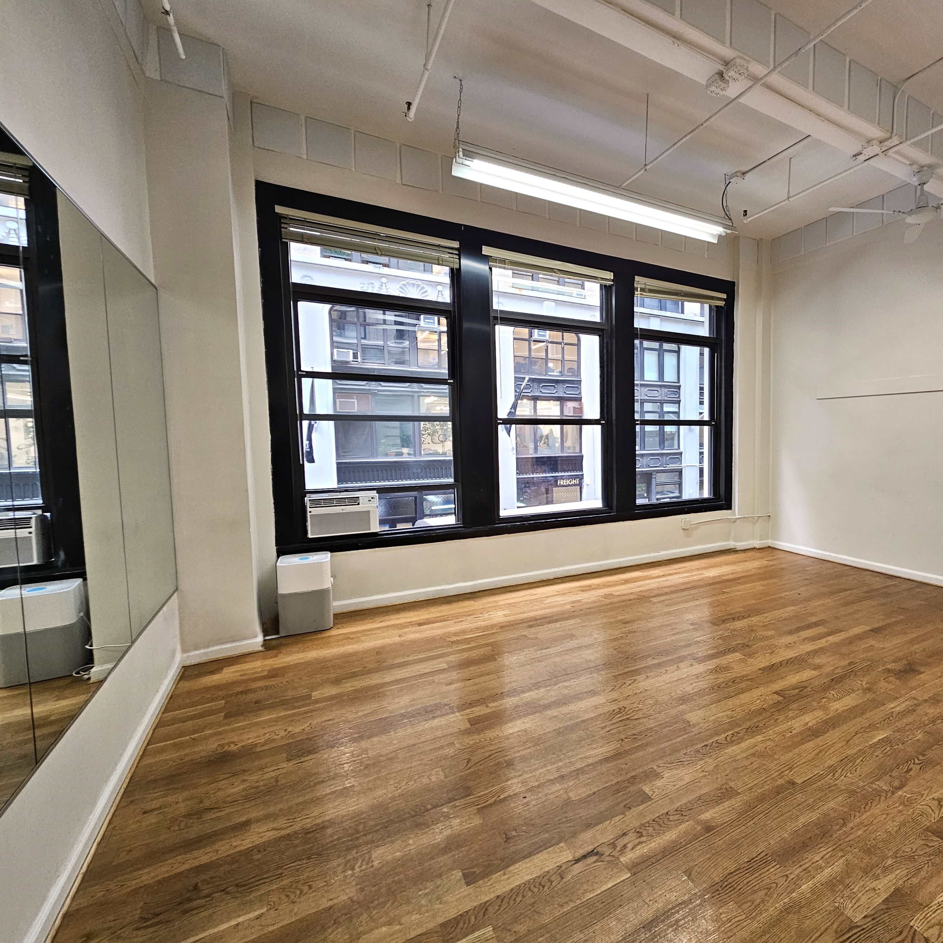 A spacious, empty room with hardwood flooring, large windows, and a blank wall.