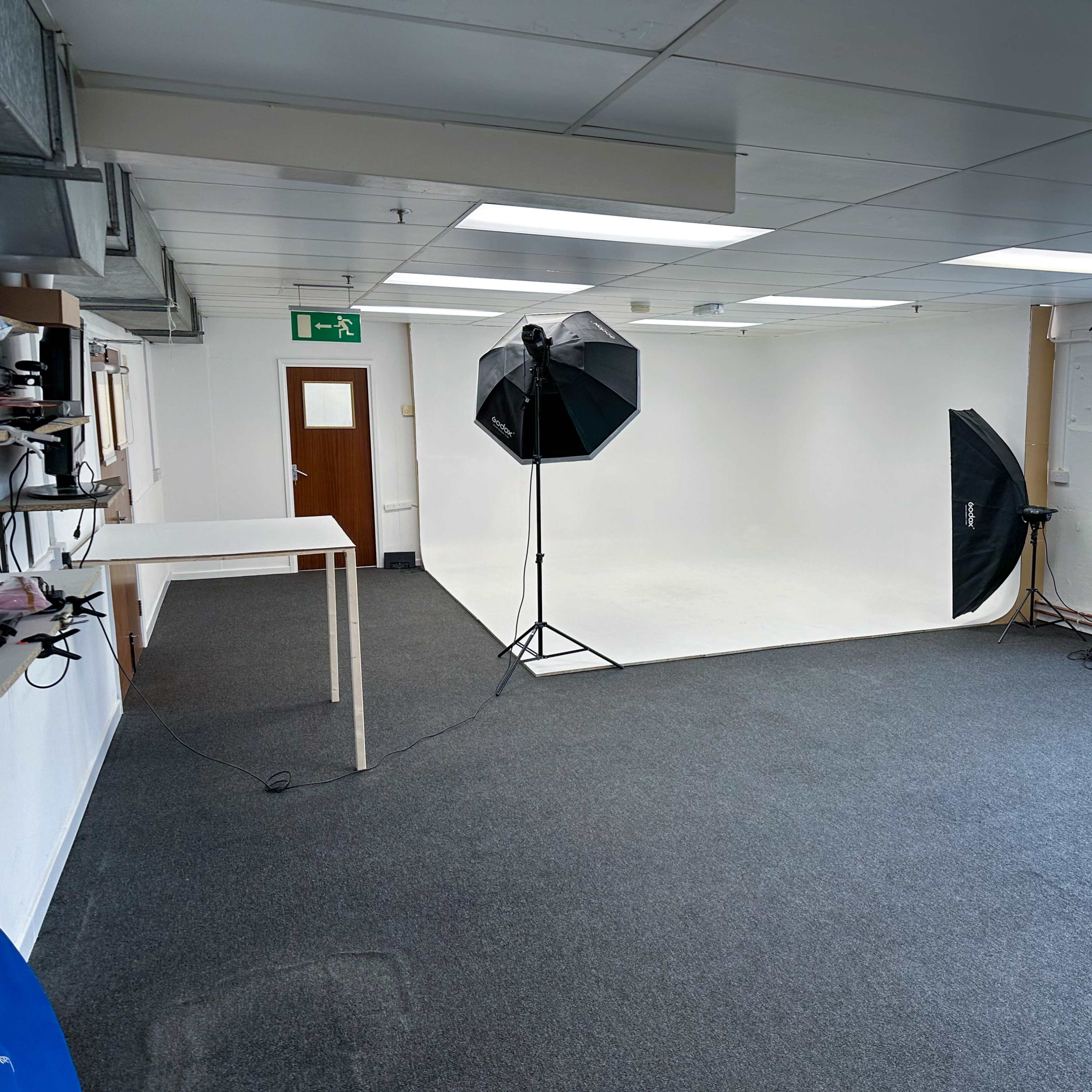 A spacious, well-lit studio with a white backdrop and photography equipment set up in a plain room.