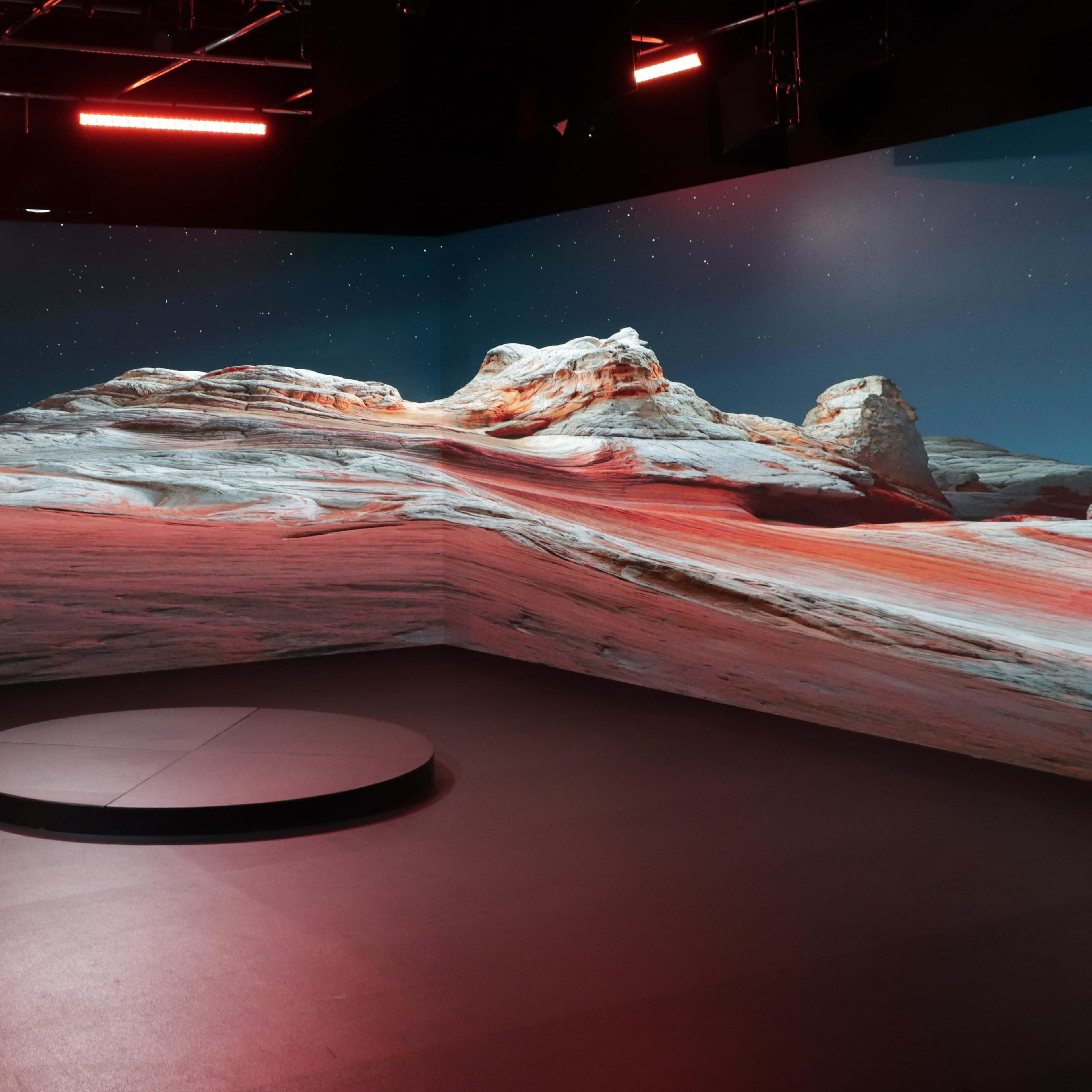A stage with a circular platform set against a backdrop of a digitally projected desert landscape under a starry sky.