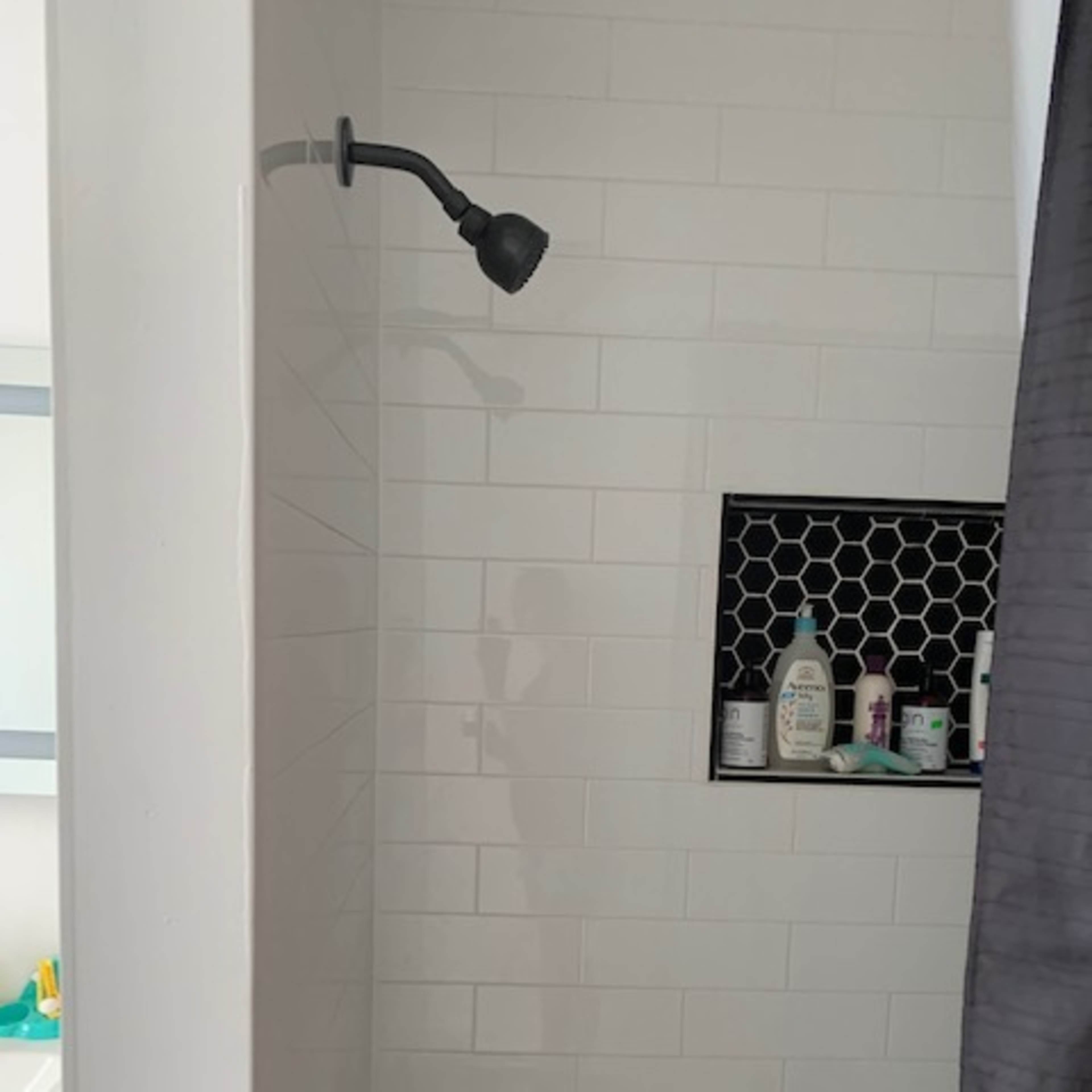 A shower with a wall-mounted showerhead, tiled white walls, and a niche containing various toiletries.