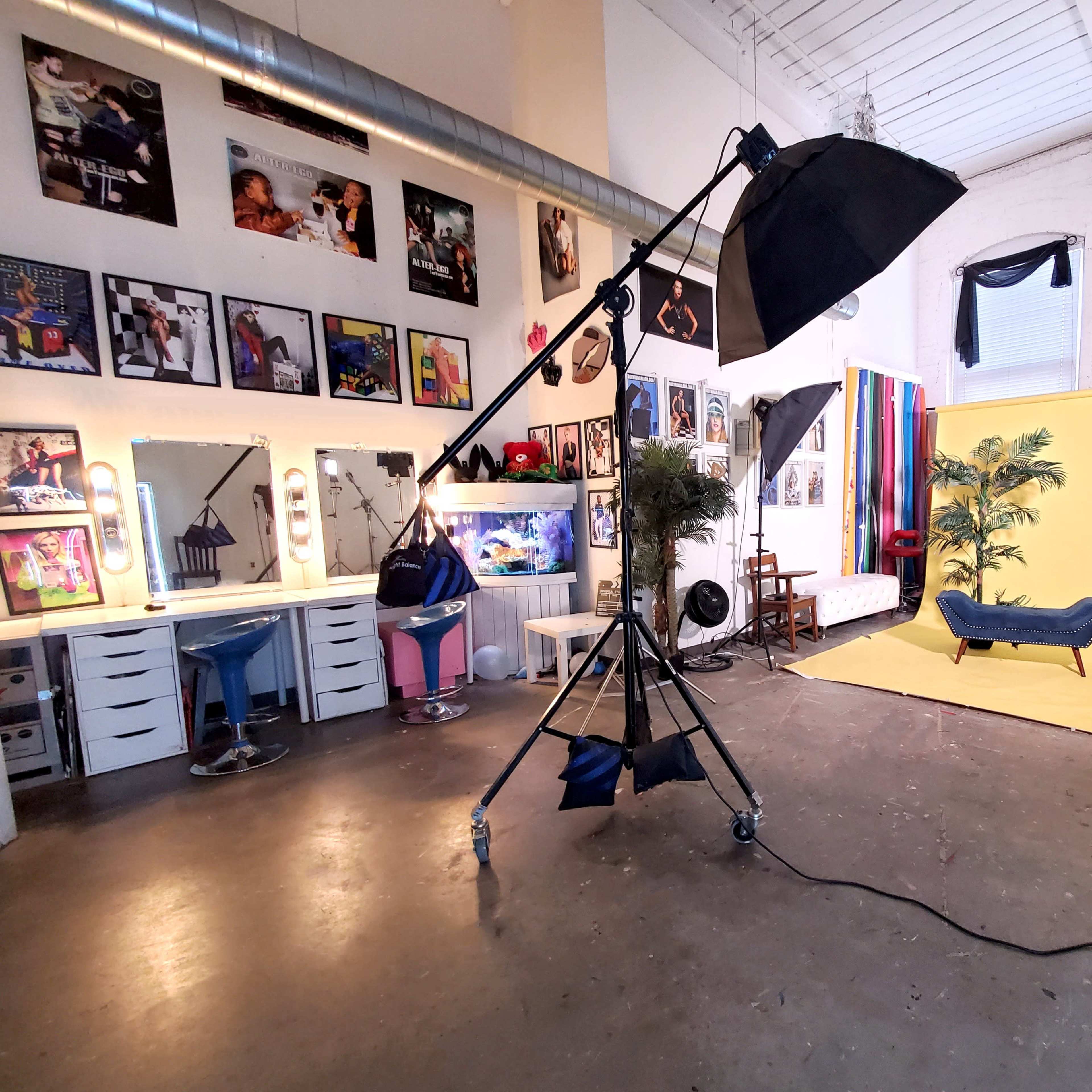 A well-lit photography studio with a yellow backdrop, various props, and equipment arranged around the space.