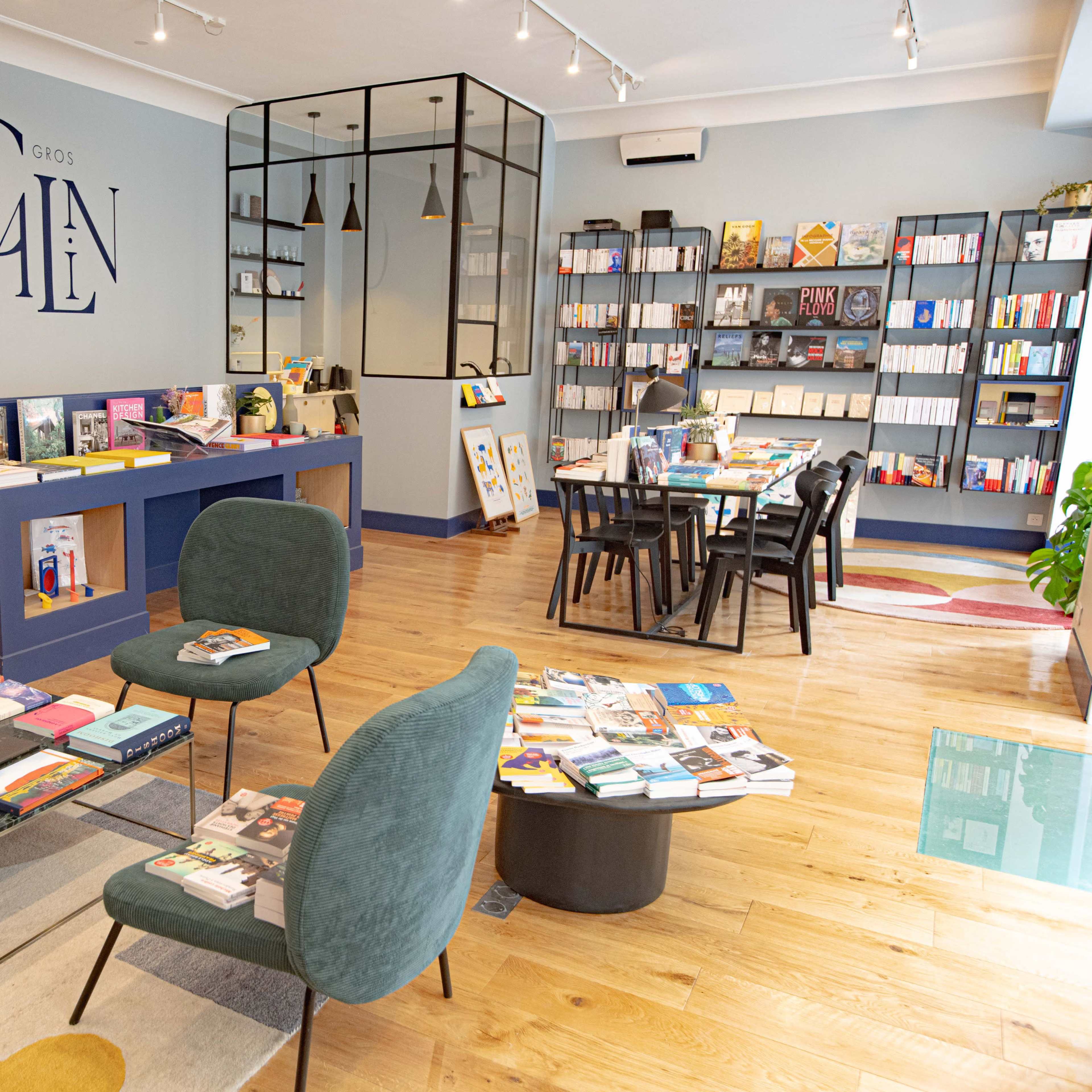 A modern bookstore interior with bookshelves lined with various titles, tables for reading, and a seating area featuring green chairs.