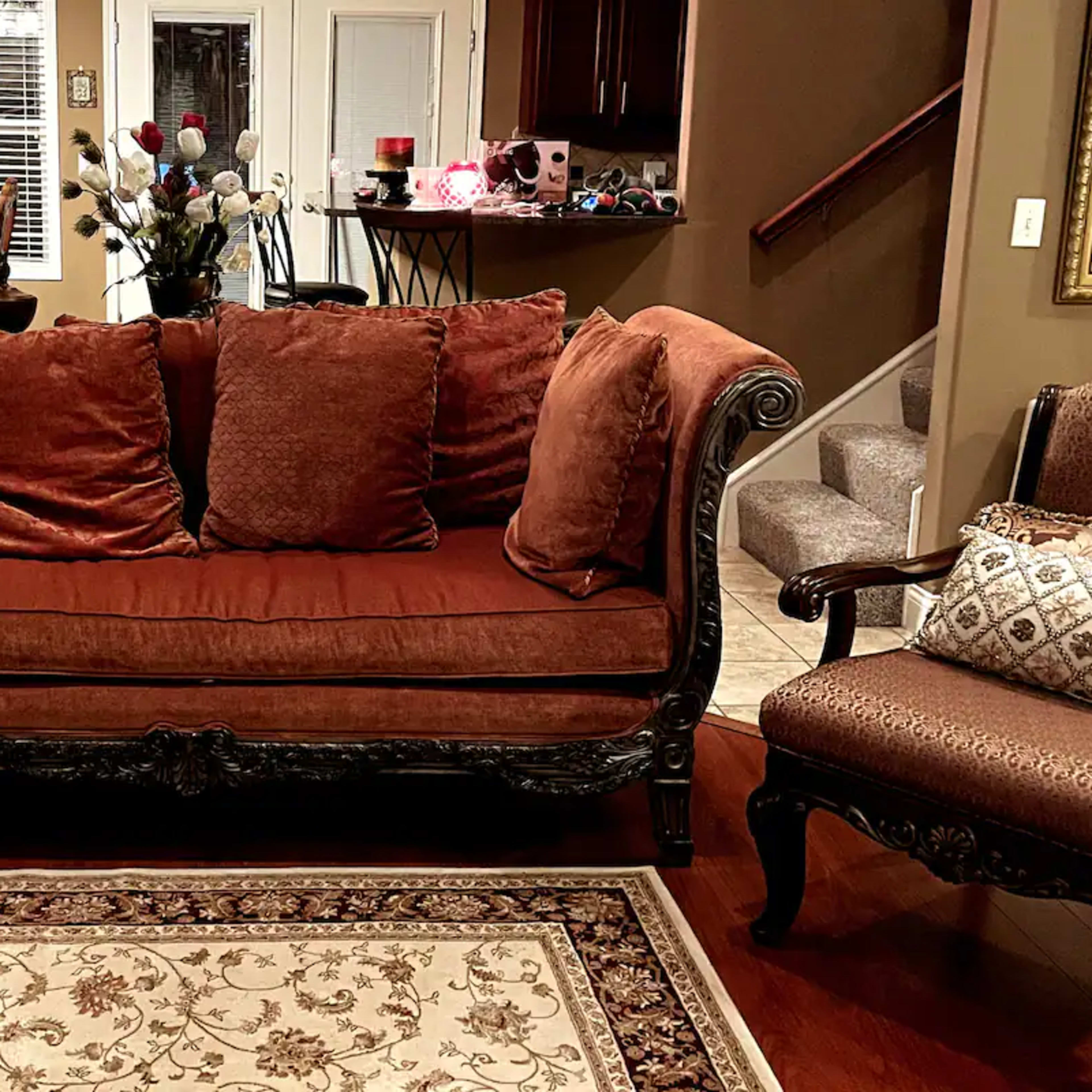 A brown sofa with large cushions, ornate wooden legs, placed on a patterned area rug in a warmly lit living room.