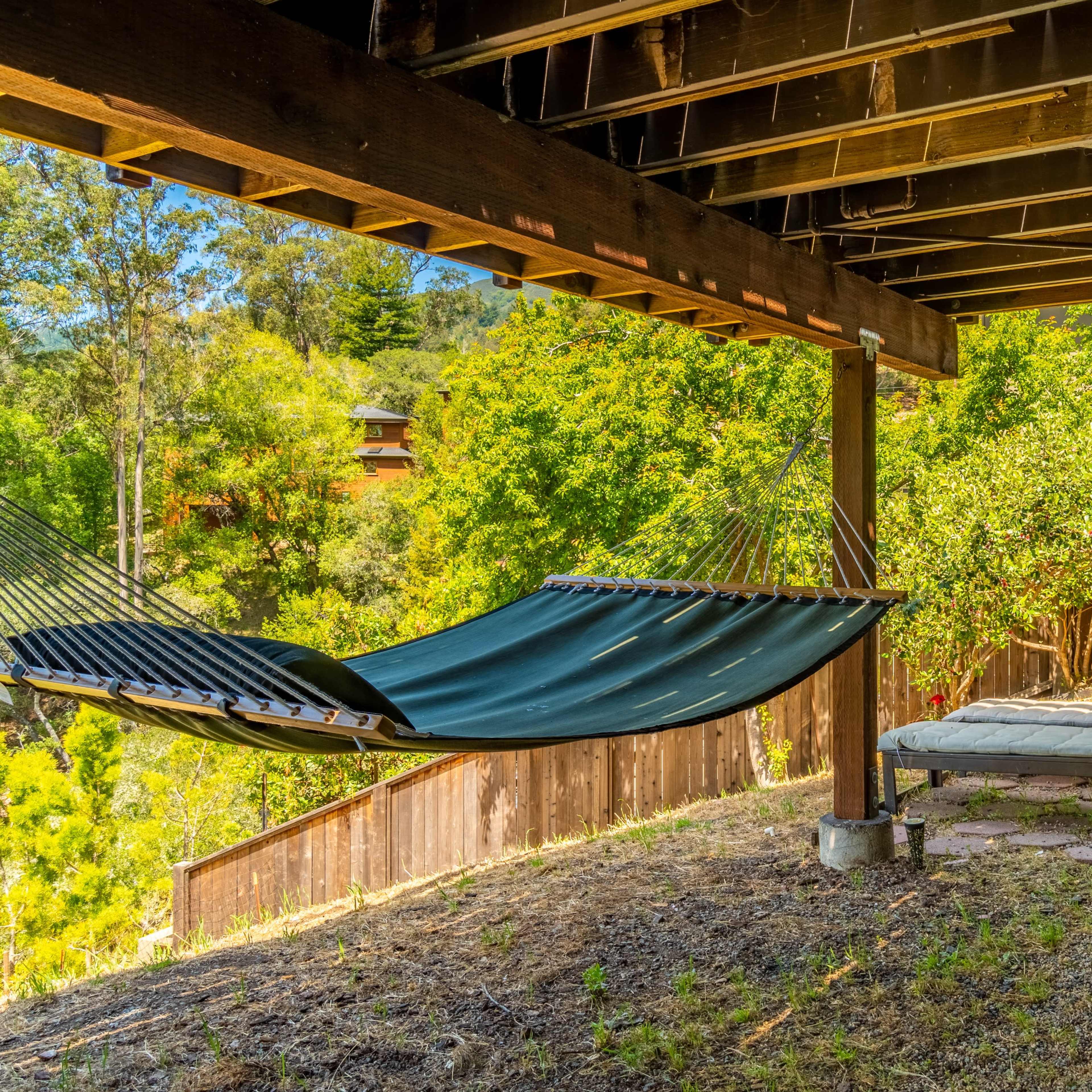 A shaded outdoor area featuring a hammock, a chaise lounge, and a small seating arrangement on stone and gravel surfaces.